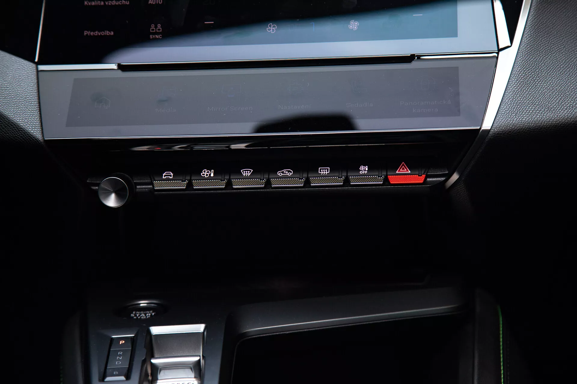 Środkowa deska rozdzielcza Peugeota 408 z 2023 r. z wyświetlaczem wyłączonego systemu infotainment dotykowego, panel kontrolny klimatyzacji z przyciskami dotykowymi oraz część obszaru elektronicznej zmiany biegów, pod delikatnym oświetleniem ambientowym podkreślającym nowoczesny, elegancki design z ciemnymi tonami i metalicznymi akcentami.
