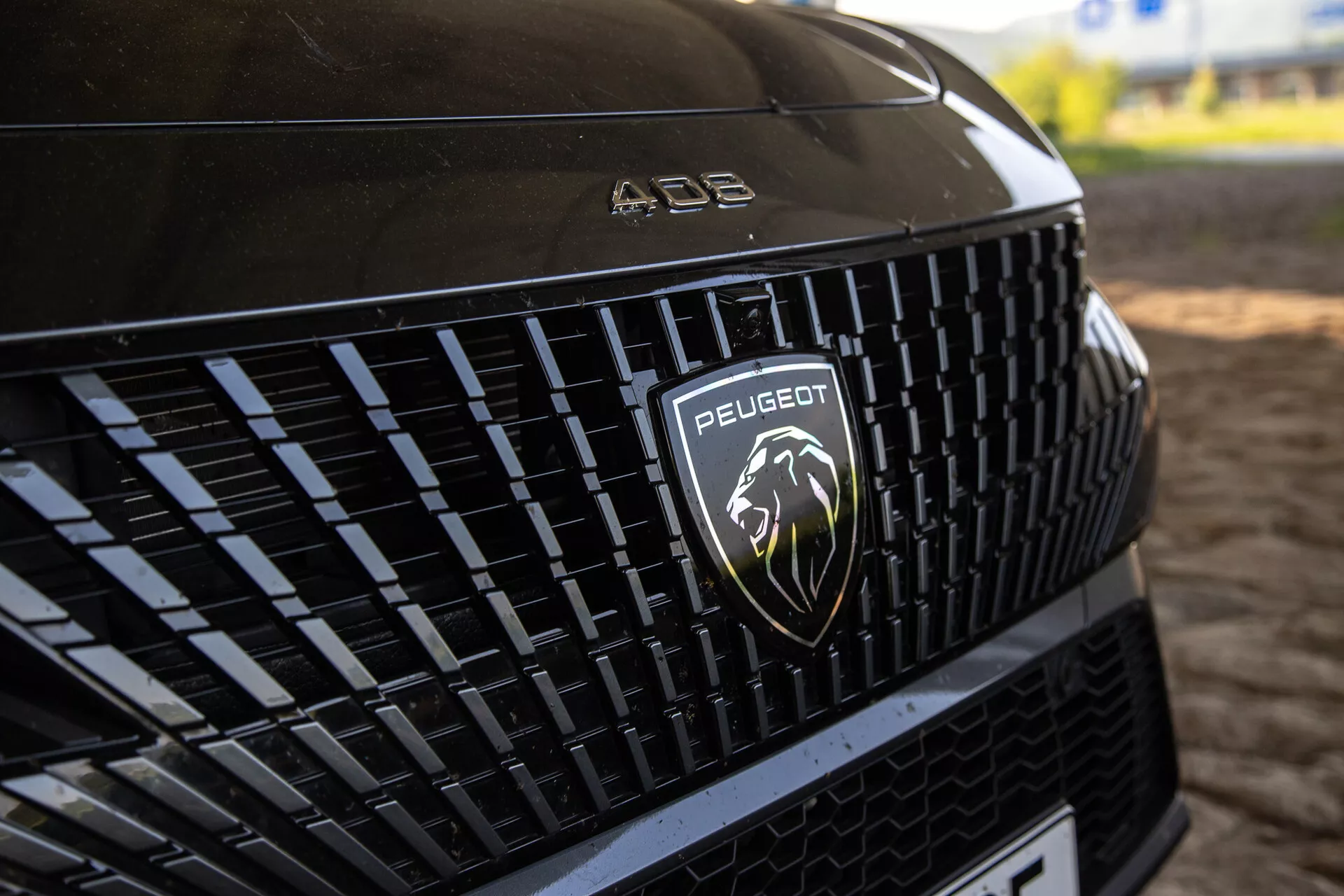 Szczegółowy widok przedniej kratki Peugeot 408 2023 pokazujący skomplikowany wzór i srebrny logo lwa, pod naturalnym oświetleniem