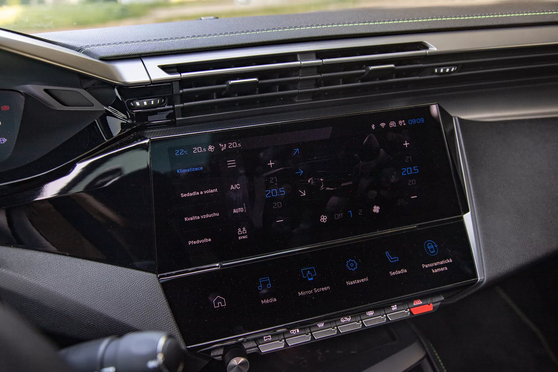 Zbliżenie na system infotainment w Peugeot 408 2023 pokazujący 8-10 calowy ekran dotykowy z nawigacją, kontrolą klimatu, ikonami odtwarzania mediów i widokiem części deski rozdzielczej, wykonane z boku pasażera