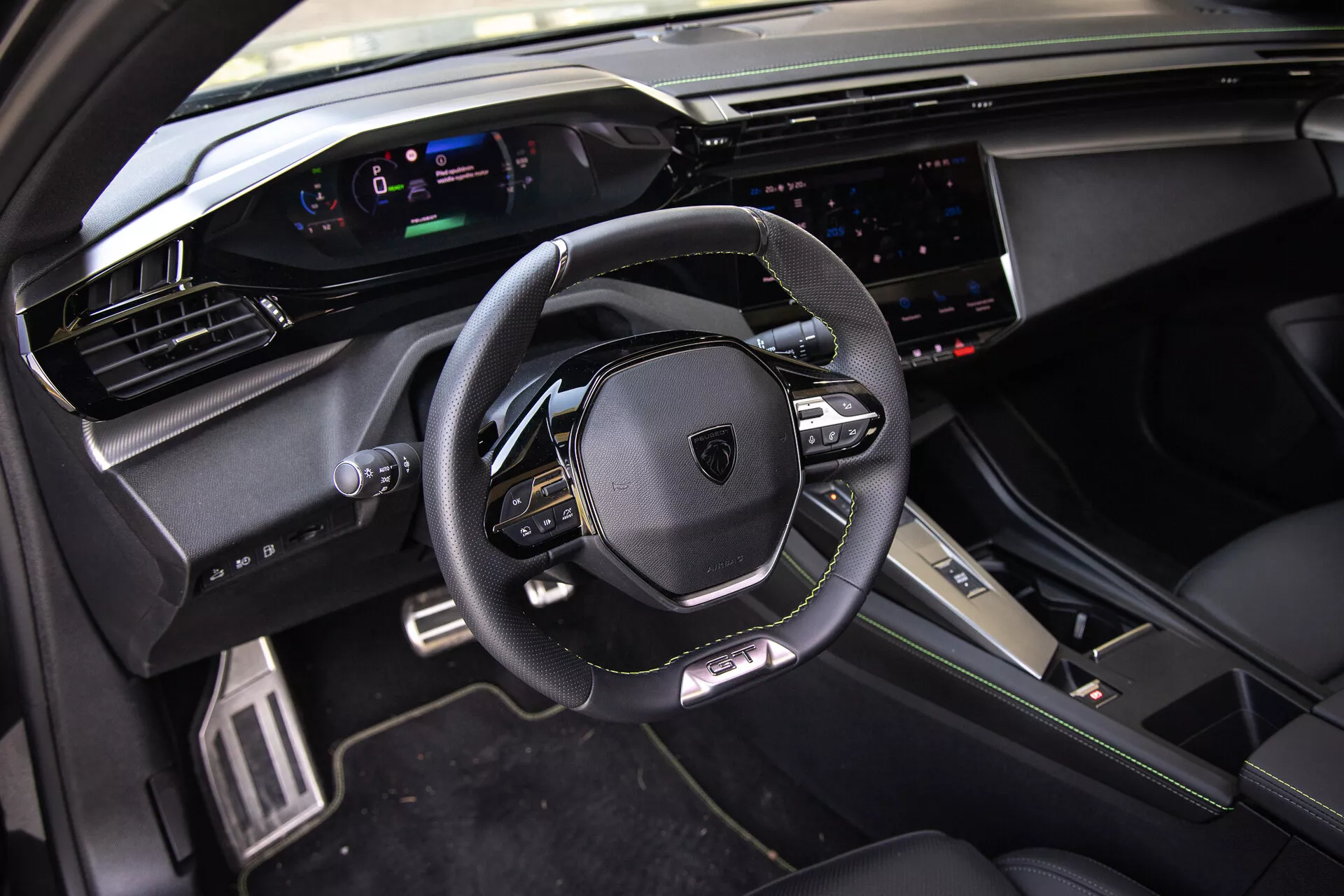 Wnętrze Peugeota 408 z 2023 roku z wielofunkcyjną kierownicą pokrytą skórą, cyfrowym zestawem wskaźników, szerokim systemem infotainment z ekranem dotykowym i sportowymi, premium elementami projektu pod naturalnym światłem z perspektywy przedniego pasażera.