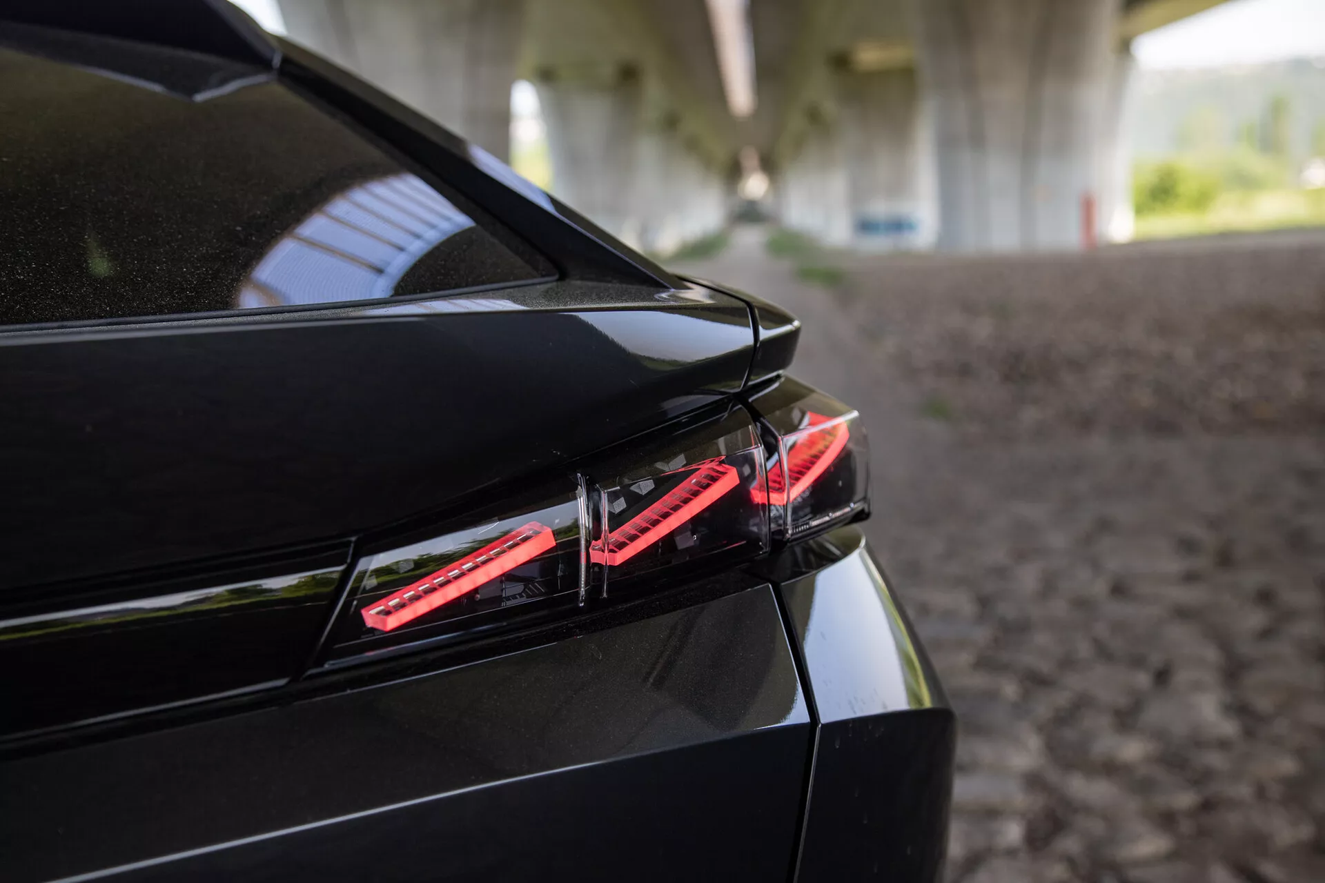 Zbliżenie na tylną część Peugeota 408 z 2023 roku z lampą tylną LED, eleganckim designem bagażnika ze zintegrowanym spoilerm i błyszczącym czarnym wykończeniem pod strukturalnym cieniem