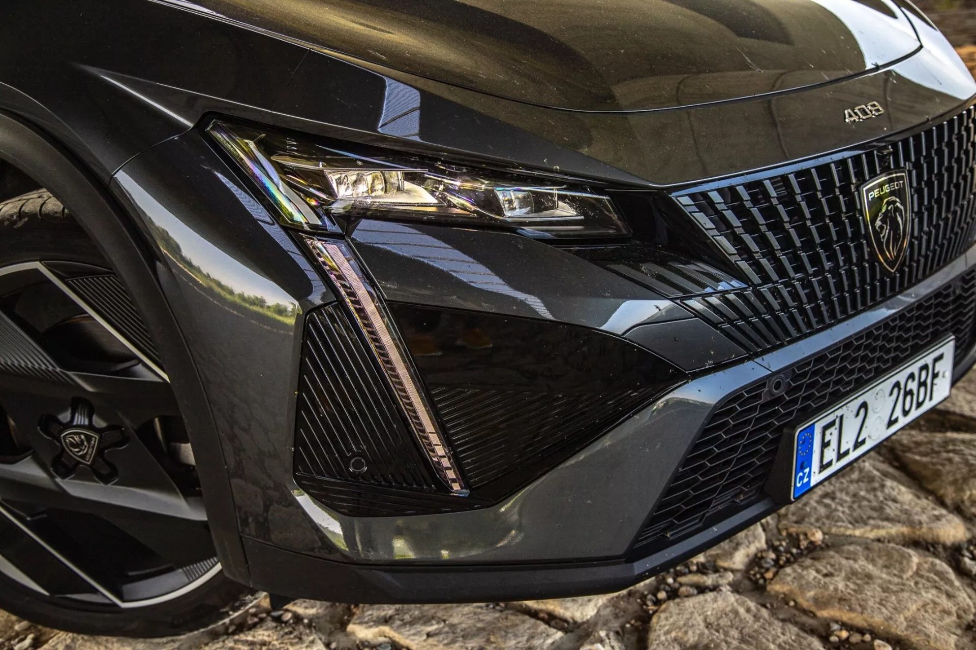 Zbliżenie na przedni lewy róg Peugeota 408 z 2023 roku pokazujące szczegółowy zespół reflektora, część grilla, maskę i koło z nowoczesną technologią LED i luksusowymi elementami designu.