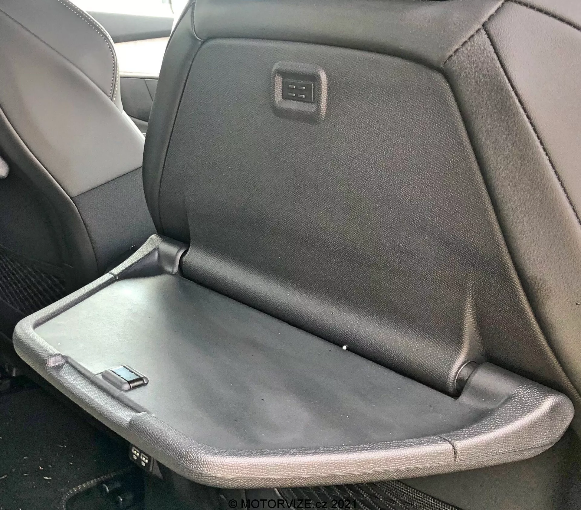 Wnętrze Peugeot 5008 2021 z tylnym siedzeniem wyposażonym w składany podłokietnik lub stolik, z tapicerką łączącą tkaninę i skórę oraz zintegrowanym ekranem lub panelem sterowania z tyłu zagłówka przedniego siedzenia.
