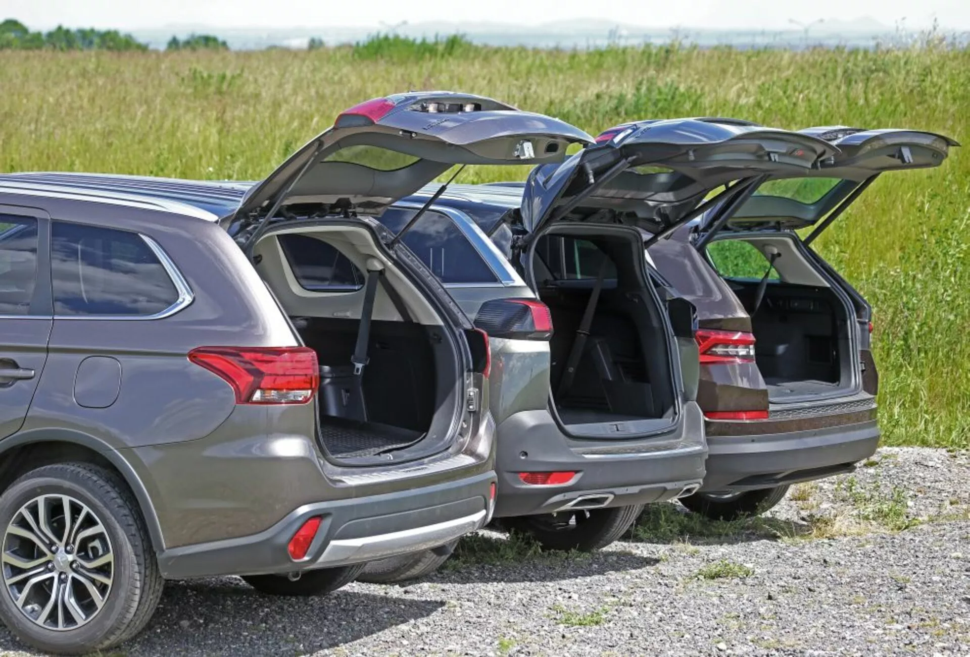 Tylny widok trzech SUV-ów Peugeot 5008 z 2013 roku zaparkowanych obok siebie, prezentujących ich automatyczne klapy bagażnika, anteny satelitarne i koła ze stopów lekkich na tle wiejskim w naturalnym świetle dziennym