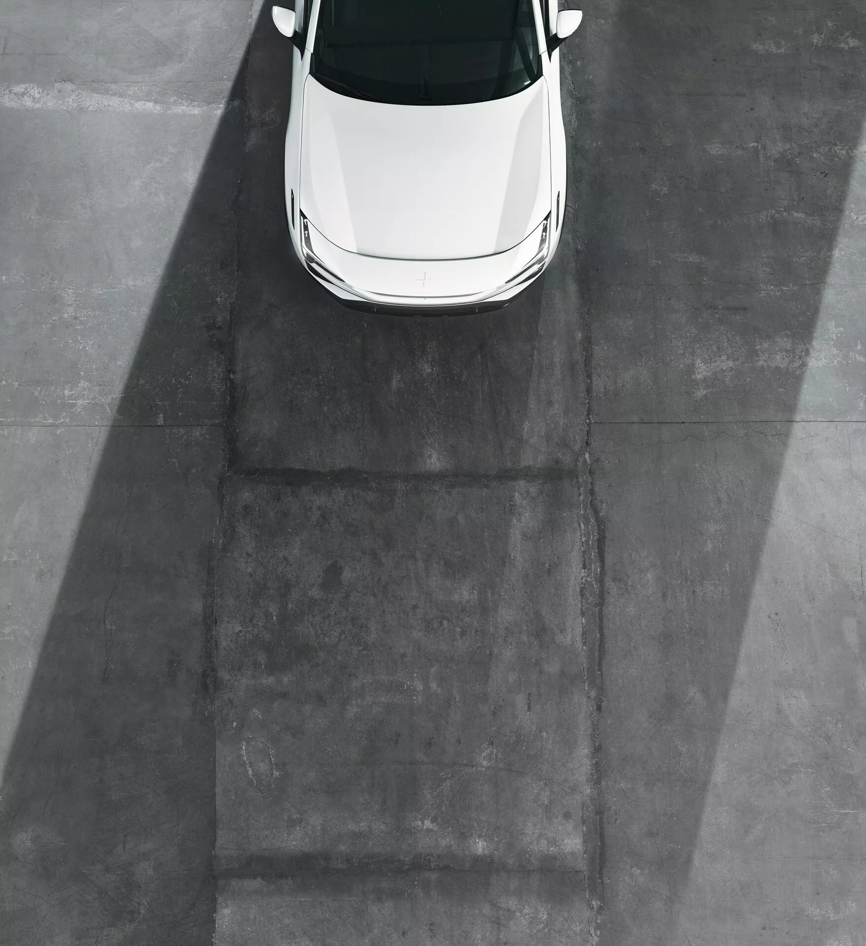 Biały model Polestar 3 2023 ujęty z lotu ptaka, wyeksponowano dach, maskę i część przedniej szyby na szarym betonowym podłożu bez widocznych kół czy boków, co wskazuje na oświetlenie wczesnym rankiem lub późnym popołudniem