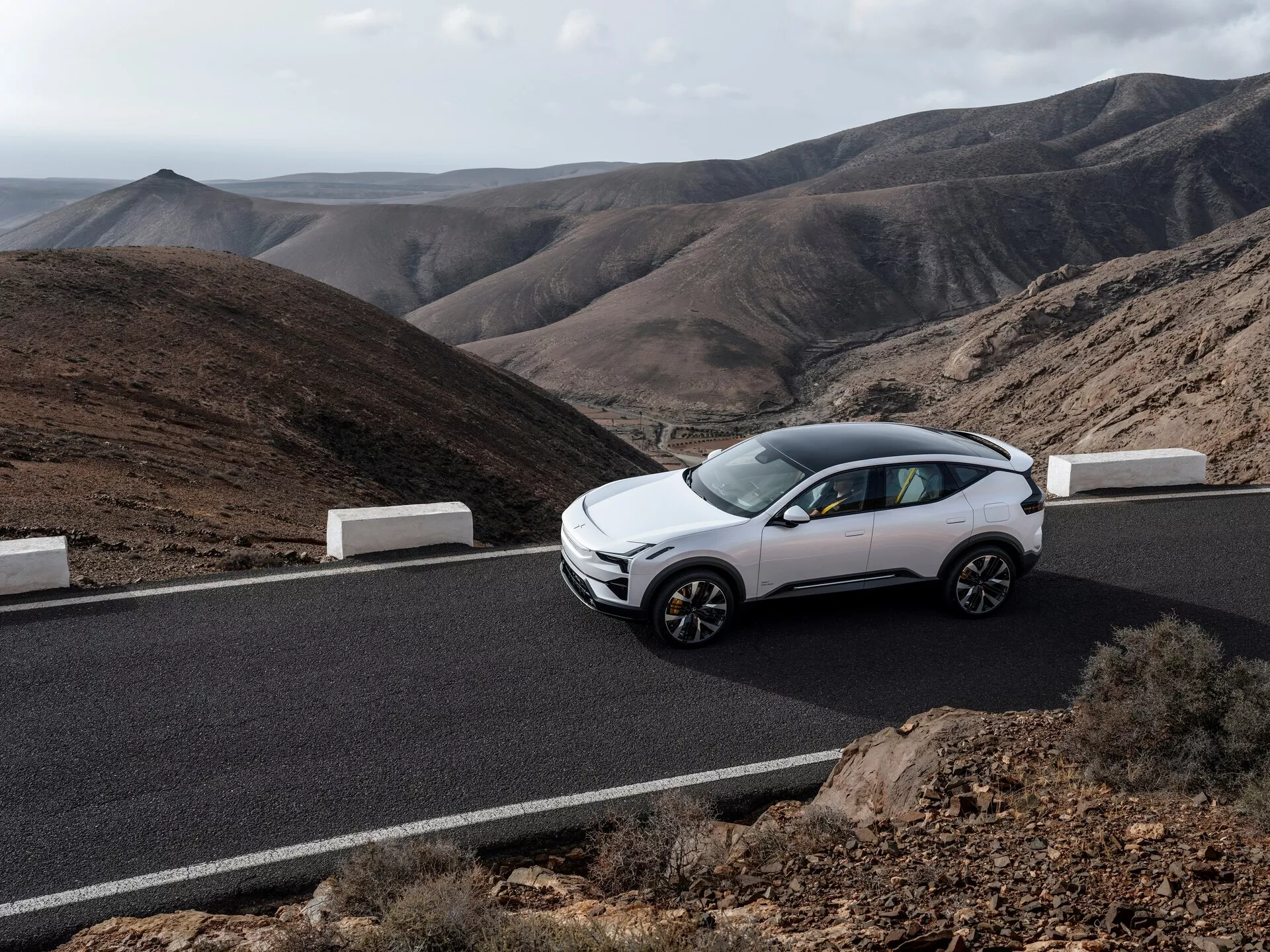 Polestar 3 pierwszej generacji 2023, kolor biały, widok z bocznego przedniego kąta na asfaltowej drodze z górami w tle, podkreślający nowoczesny design crossovera, cechy kompaktowego SUV-a oraz felgi aluminiowe pod naturalnym światłem.