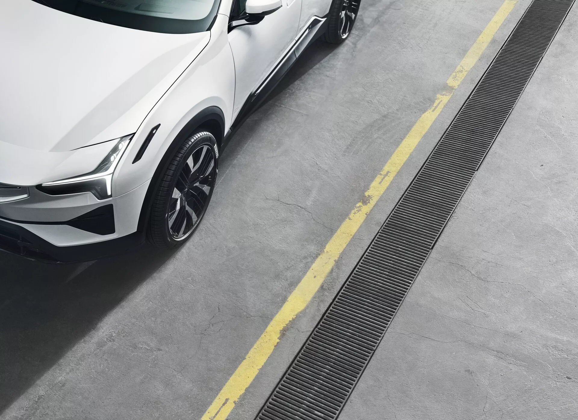 Polestar 3 z 2023 roku, 1. generacja, widziany z górnego kąta, pokazujący przedni prawy kwadrant, w tym reflektor LED, metaliczny lakier, koło z lekkich stopów o wieloramiennej konstrukcji oraz dynamiczne linie karoserii na czystej betonowej nawierzchni z żółtymi liniami parkingowymi.