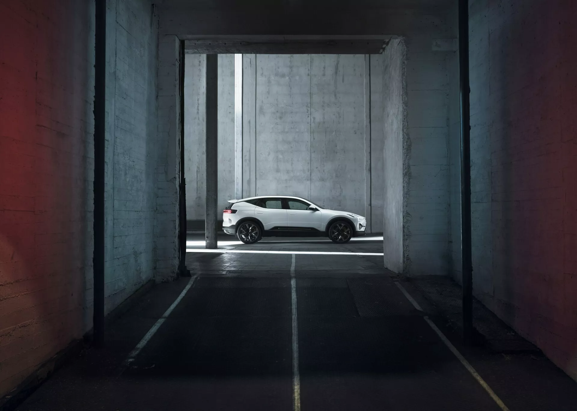Polestar 3 1. generacji z 2023 roku w kolorze białym, prezentujący swój elegancki profil boczny w dramatycznie oświetlonym garażu, podkreślający sportowe felgi aluminiowe, gładkie linie aerodynamiczne karoserii i przyciemniane szyby dla nowoczesnego wyglądu luksusowego coupé.