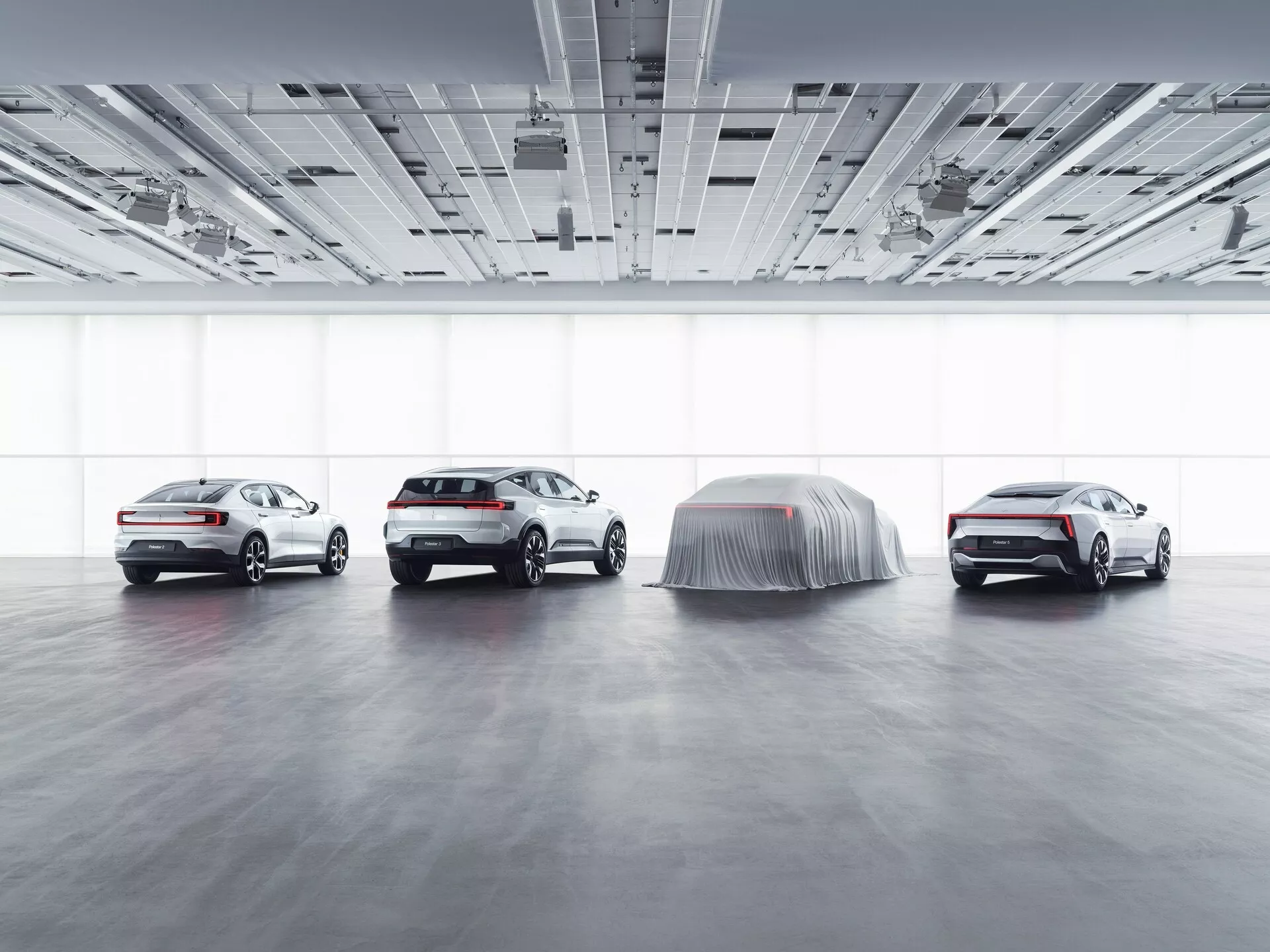 Wystawa Polestar 3 2023 w salonie z rozproszonym oświetleniem, prezentująca widoki z boku i z przodu na trzy widoczne samochody oraz jeden model pokryty, sugerujący prezentację, ilustrująca zaawansowane funkcje technologiczne