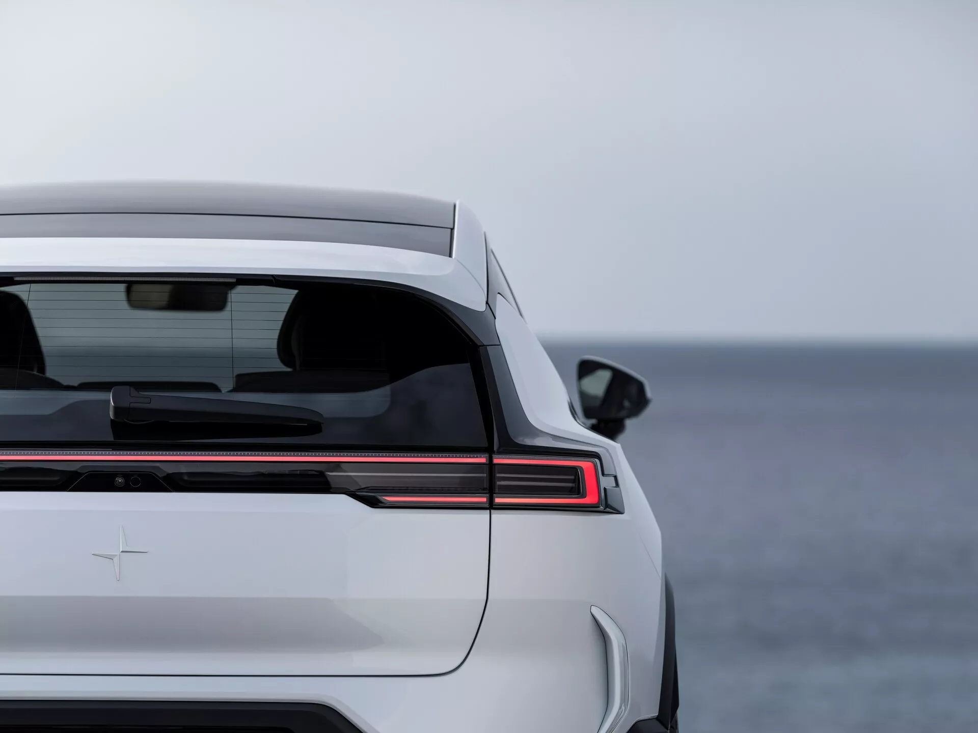 Polestar 3 1. generacji z 2023 roku prezentująca elementy designu tylnej części, w tym poziomy pasek świateł LED, przyciemniane tylne okno z funkcją odmgławiania, zintegrowany spoiler bagażnika i premium odznakę na tle otwartych wód.