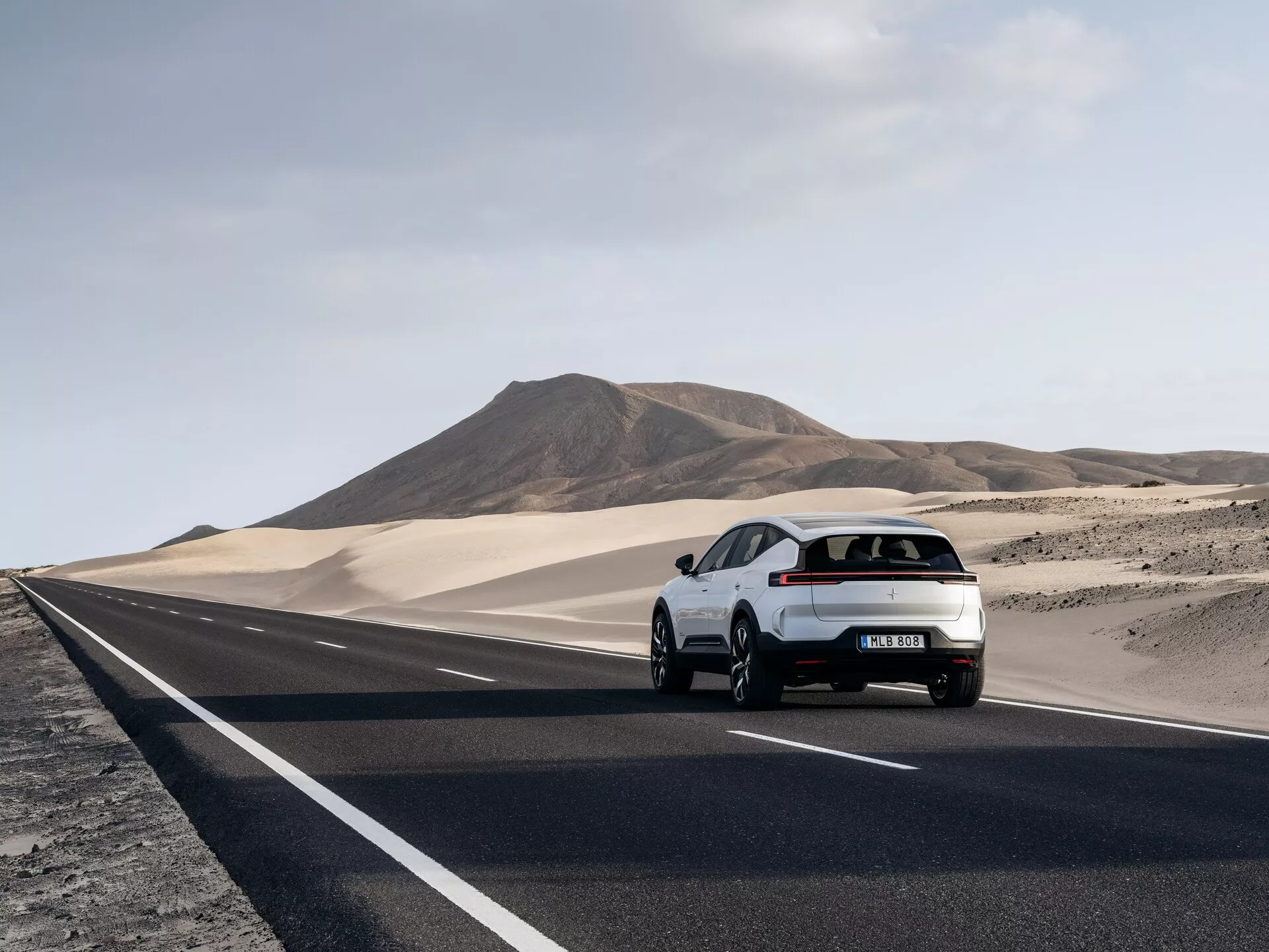 Hatchback Polestar 3 z 2023 roku jadący po pustynnej drodze, prezentujący swoją lewą stronę tylną i aerodynamiczny design z tylnymi światłami LED
