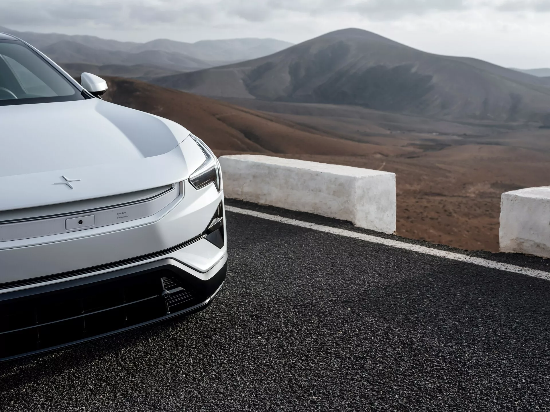 Zbliżenie na przednią część sedana Polestar 3 2023 z zaawansowaną aerodynamiką, projektem pojazdu elektrycznego z reflektorami LED i górskim krajobrazem w tle