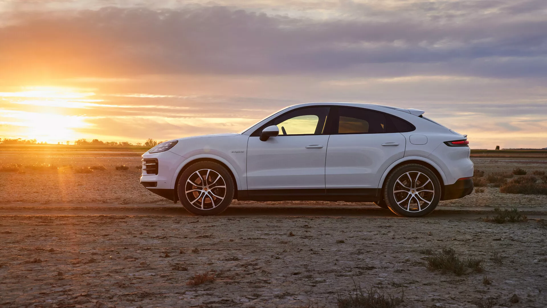 Luksusowy crossover SUV Porsche Cayenne 2023 w lśniącej bieli na jałowym terenie o złotej godzinie, prezentujący widok z boku, sportowe felgi aluminiowe i eleganckie cechy wzornictwa
