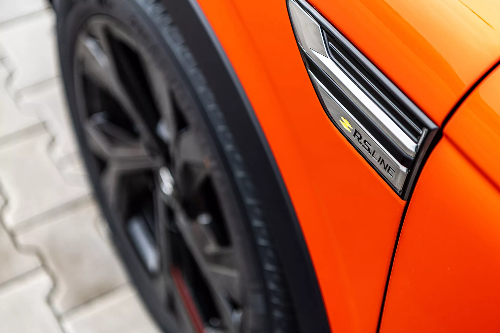 Zbliżenie pomarańczowego Renault Arkana 2021 pokazujące profil boczny z naciskiem na odznakę S-Line, błotnik i sportowy wzór koła z niskiego kąta