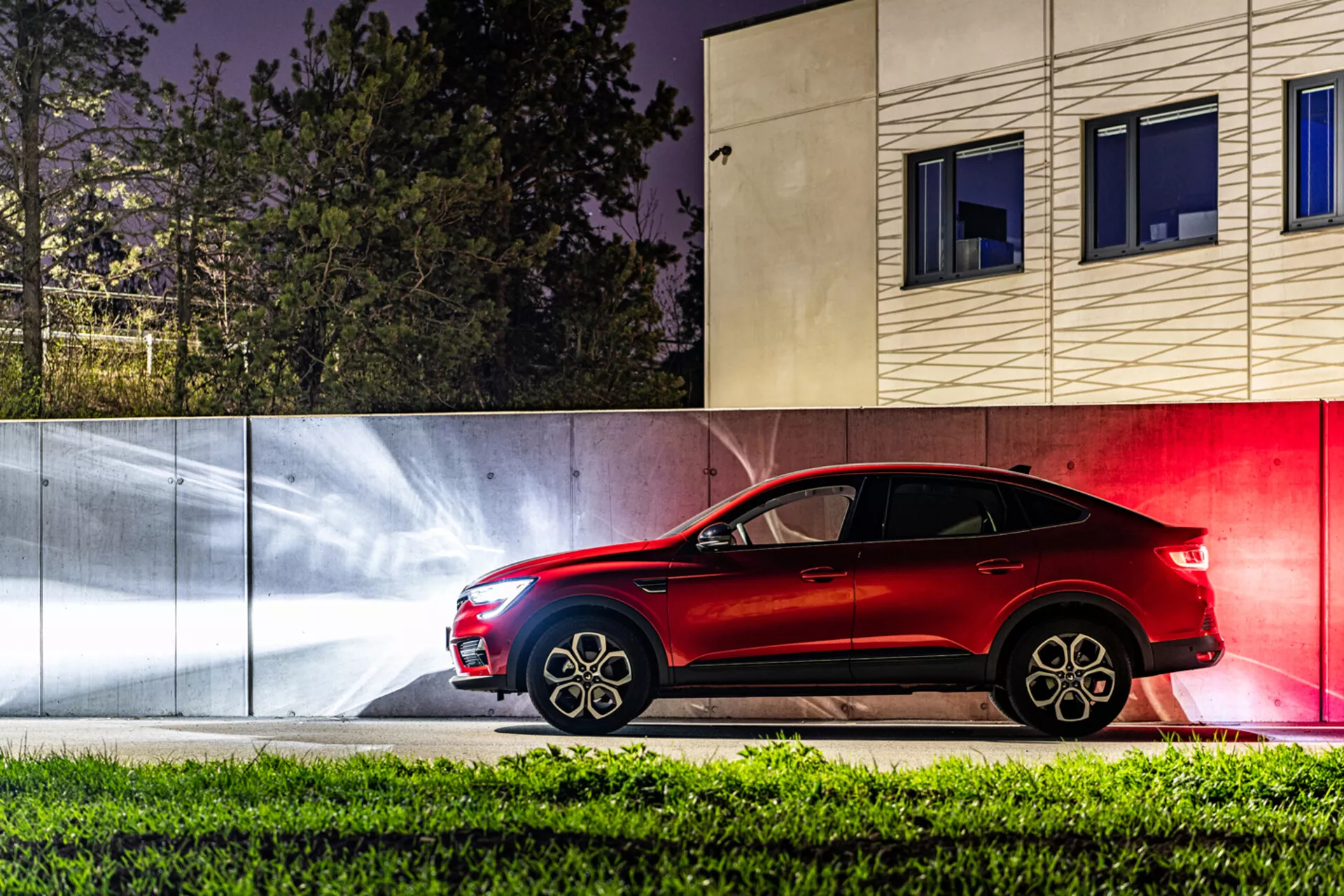 Widok boczny Renault Arkana 2021 w nocy z dynamicznymi smugami świetlnymi i współczesnym miejskim tłem, ukazujący jego elegancki design SUVa o linii coupé i zaawansowaną technologię oświetleniową.