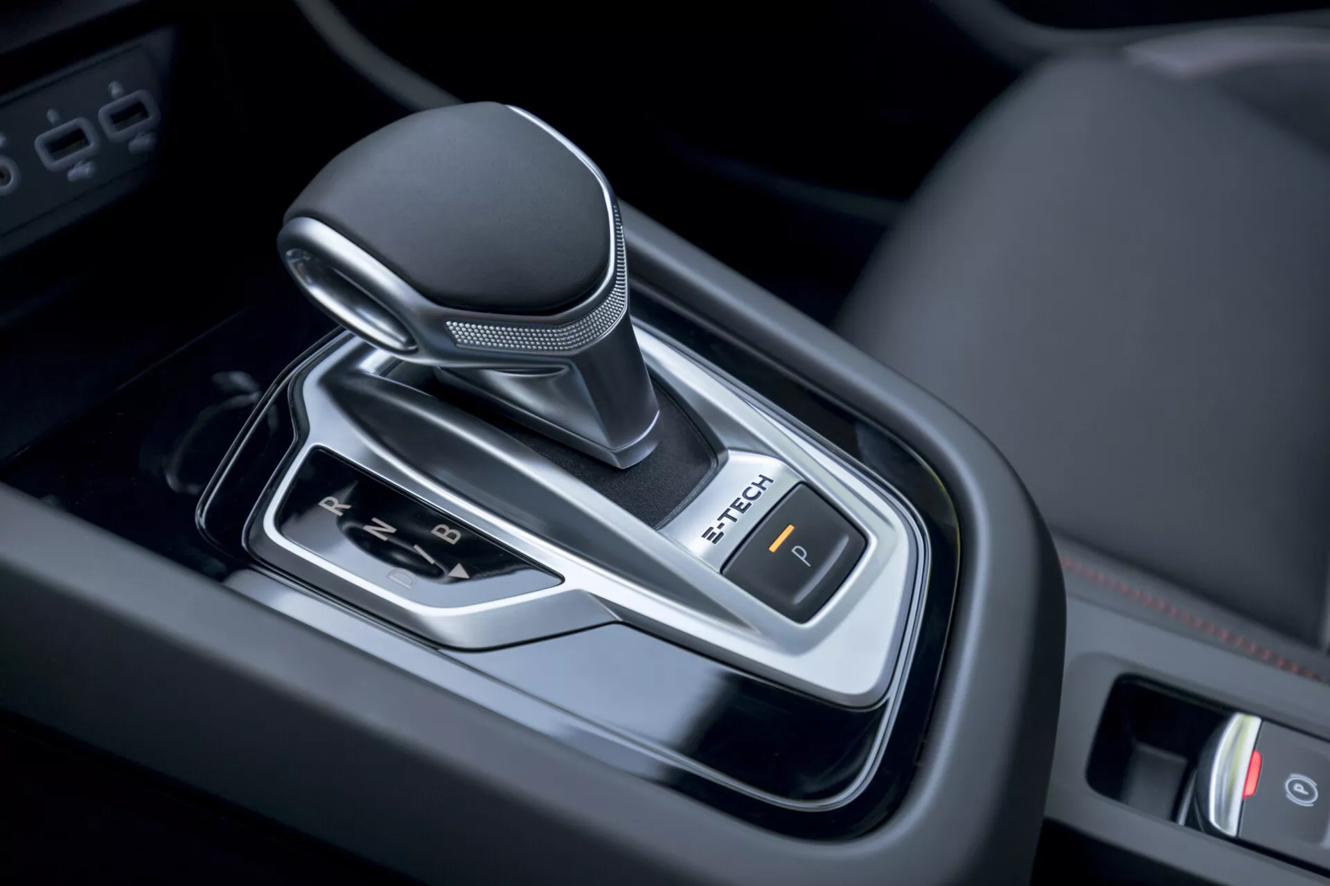 Zbliżenie na dźwignię zmiany biegów z automatyczną skrzynią biegów Renault Arkana 2021 we wnętrzu pojazdu, ukazujące nowoczesny design z pokrętłem owiniętym skórą, akcentami chromu i kontrolą elektronicznego hamulca postojowego.