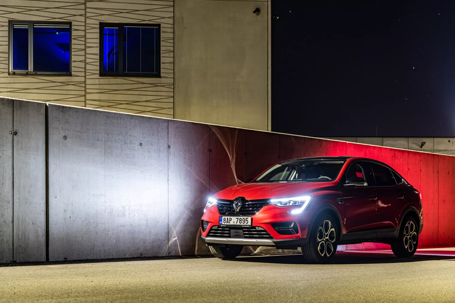 Sportowy hatchback Renault Arkana 2021 zaparkowany nocą, prezentujący reflektory LED, przedni grill oraz felgi aluminiowe pod sztucznym oświetleniem