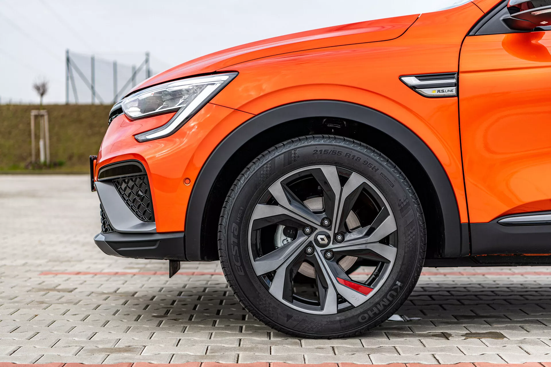 Zbliżony boczny widok pomarańczowej Renault Arkana 2021, pokazujący wieloramienne felgi aluminiowe, opony niskoprofilowe, system hamulcowy o wysokiej wydajności i LED-owe światła do jazdy dziennej