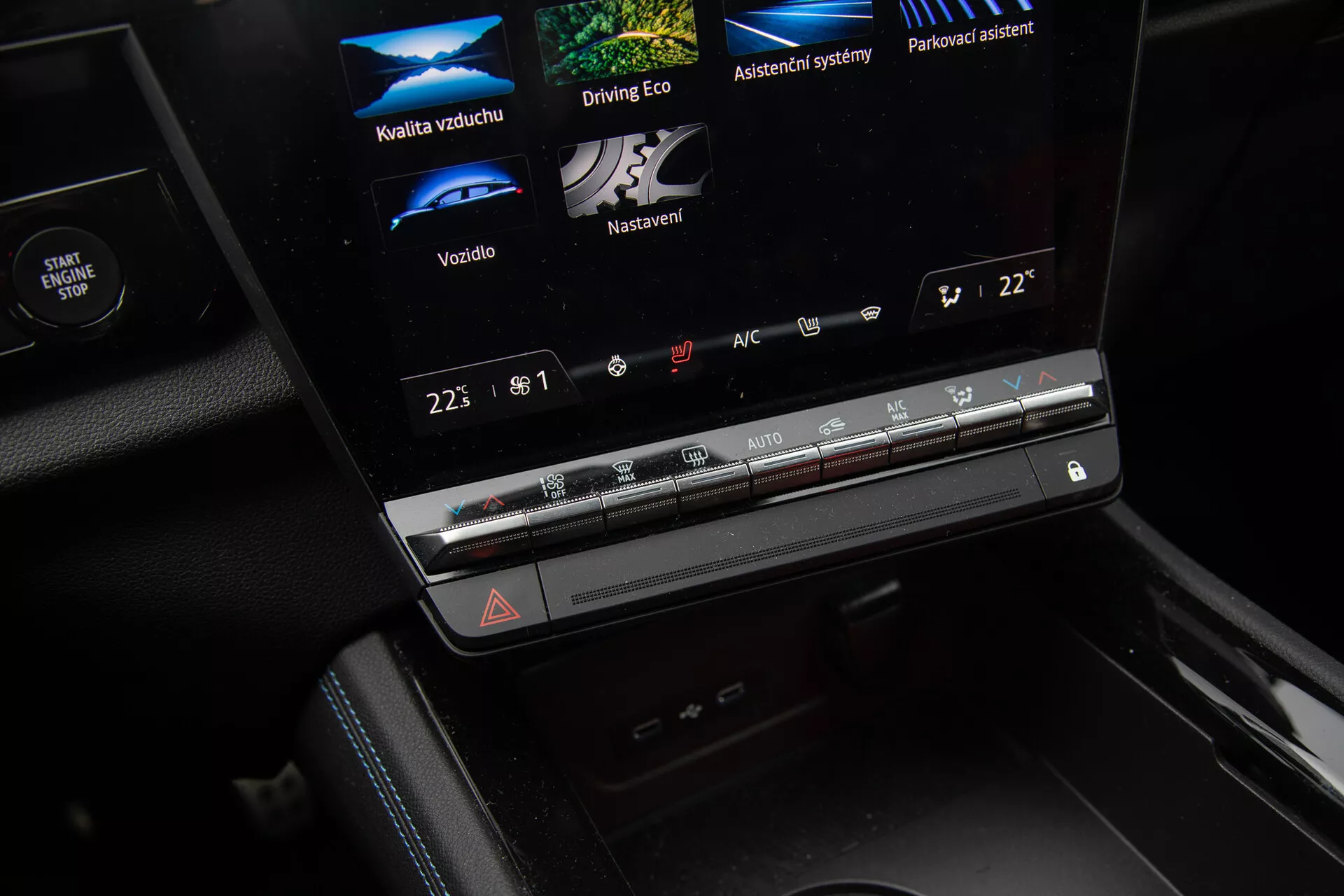 Zbliżenie wnętrza Renault Austral 2022 ukazujące konsolę środkową z ekranem dotykowym infotainment wyświetlającym opcje Jakość Powietrza, Eko Jazda, Systemy Pomocnicze i Asystent Parkowania, sterowanie klimatyzacją i przycisk awaryjnych świateł ostrzegawczych.