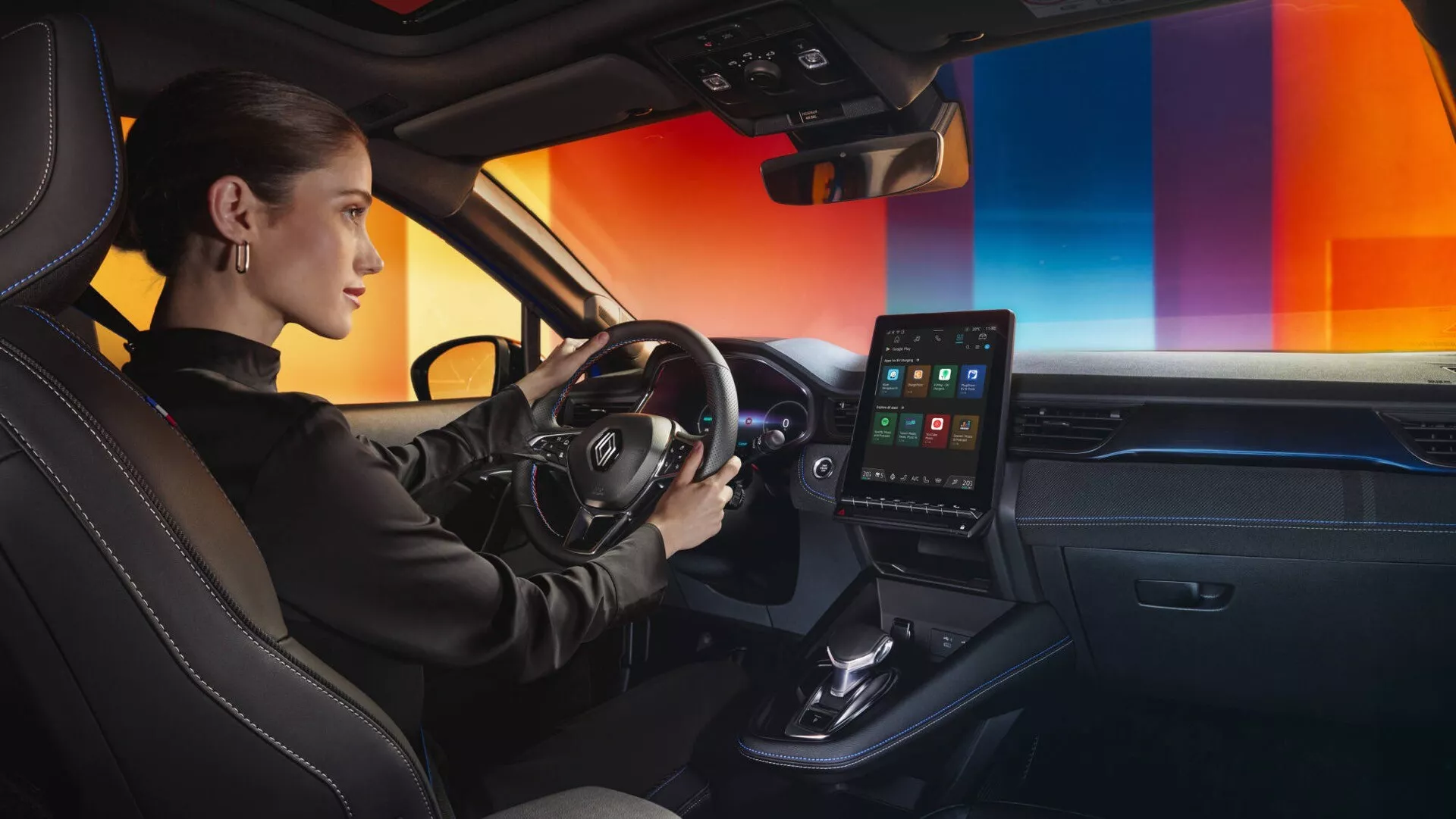 Widok wnętrza Renault Captur II-Facelift 2024 skoncentrowany na stronie kierowcy z prawo-środkowego kąta, prezentujący kierownicę z wielofunkcyjnymi przyciskami, cyfrowy zestaw wskaźników, ekran dotykowy systemu infotainment skierowany w stronę kierowcy, minimalistyczną konsolę środkową, wyloty automatycznej klimatyzacji, dźwignię zmiany biegów automatycznej skrzyni biegów, wykończenia z materiałów premium, sportowe siedzenia z skóry lub materiału skóropodobnego z kontrastowymi szwami i oświetlenie ambientowe deski rozdzielczej.