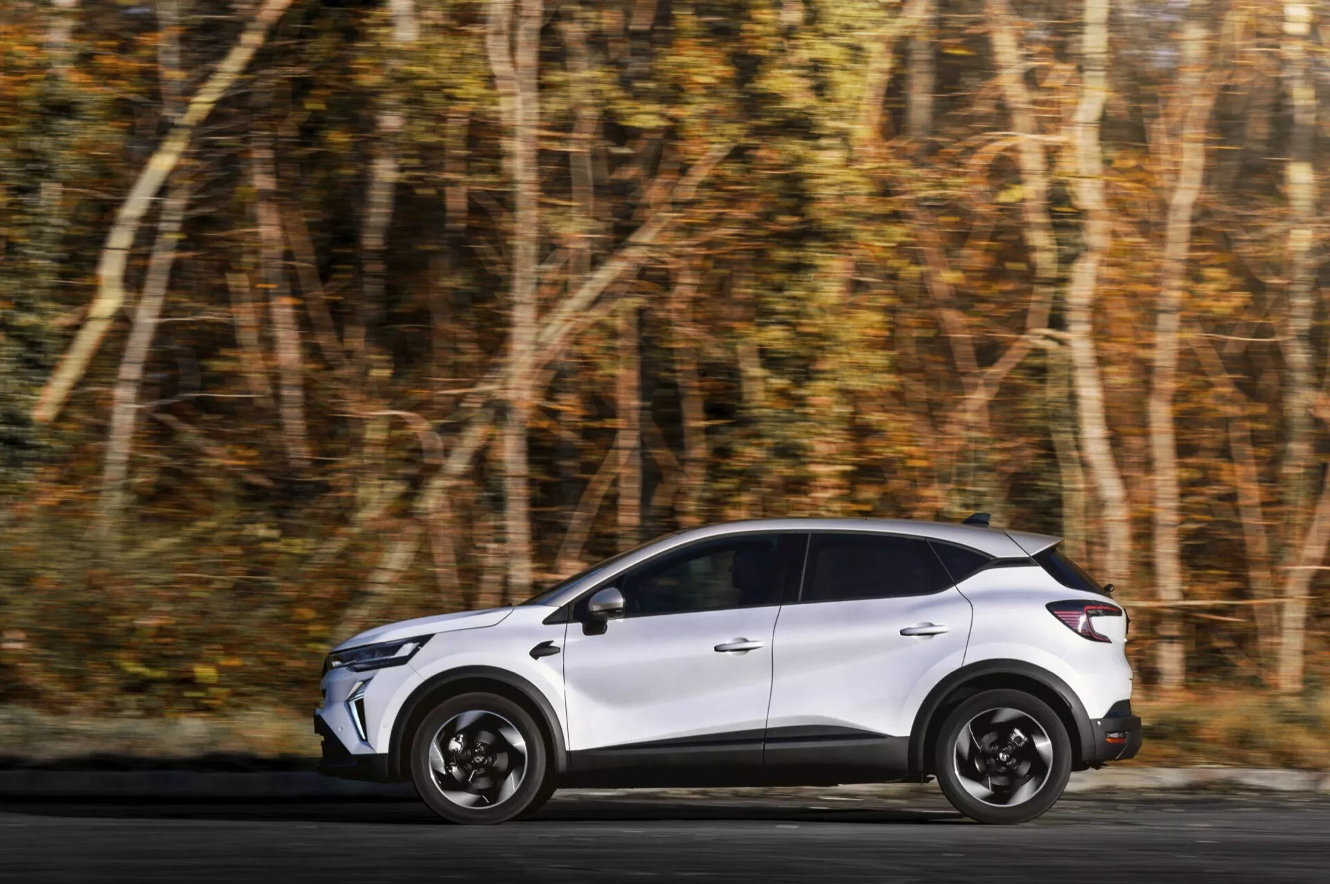 Renault Captur 2024 (II lifting) w ruchu na leśnej drodze, prezentujący swój pełny profil boczny ze smukłym designem, charakterystycznymi kołami i wglądem w elementy designu tylnej części