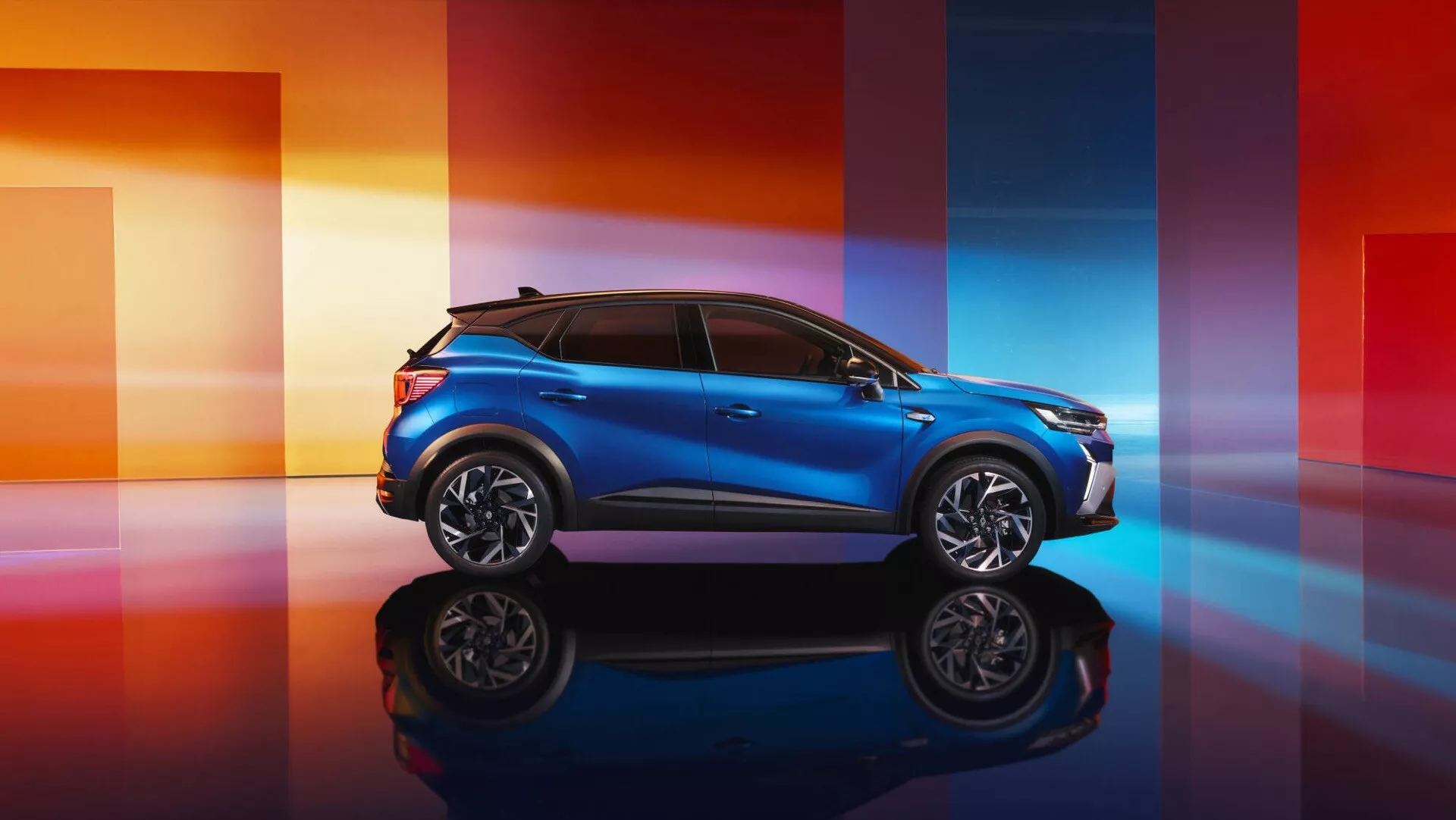 Renault Captur II lifting 2024 w kolorze niebieskim metalicznym, prezentujący sportowy profil i elegancko zaprojektowany przód na odbijającej powierzchni z dynamicznym, gradientowym tłem