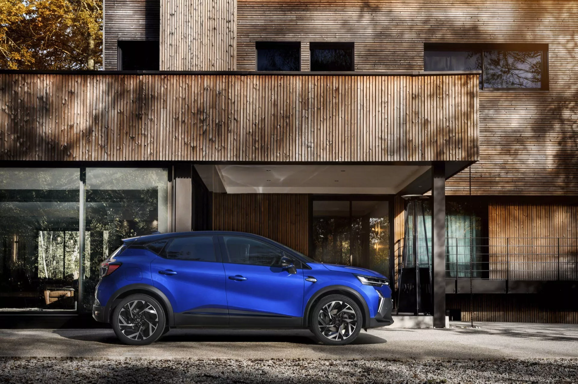 Renault Captur II Facelift 2024 w jasnym niebieskim kolorze, widok z profilu bocznego z LEDowymi reflektorami i felgami ze stopu lekkiego przed współczesnym budynkiem mieszkalnym, prezentujących cechy projektu samochodowego i systemu oświetlenia