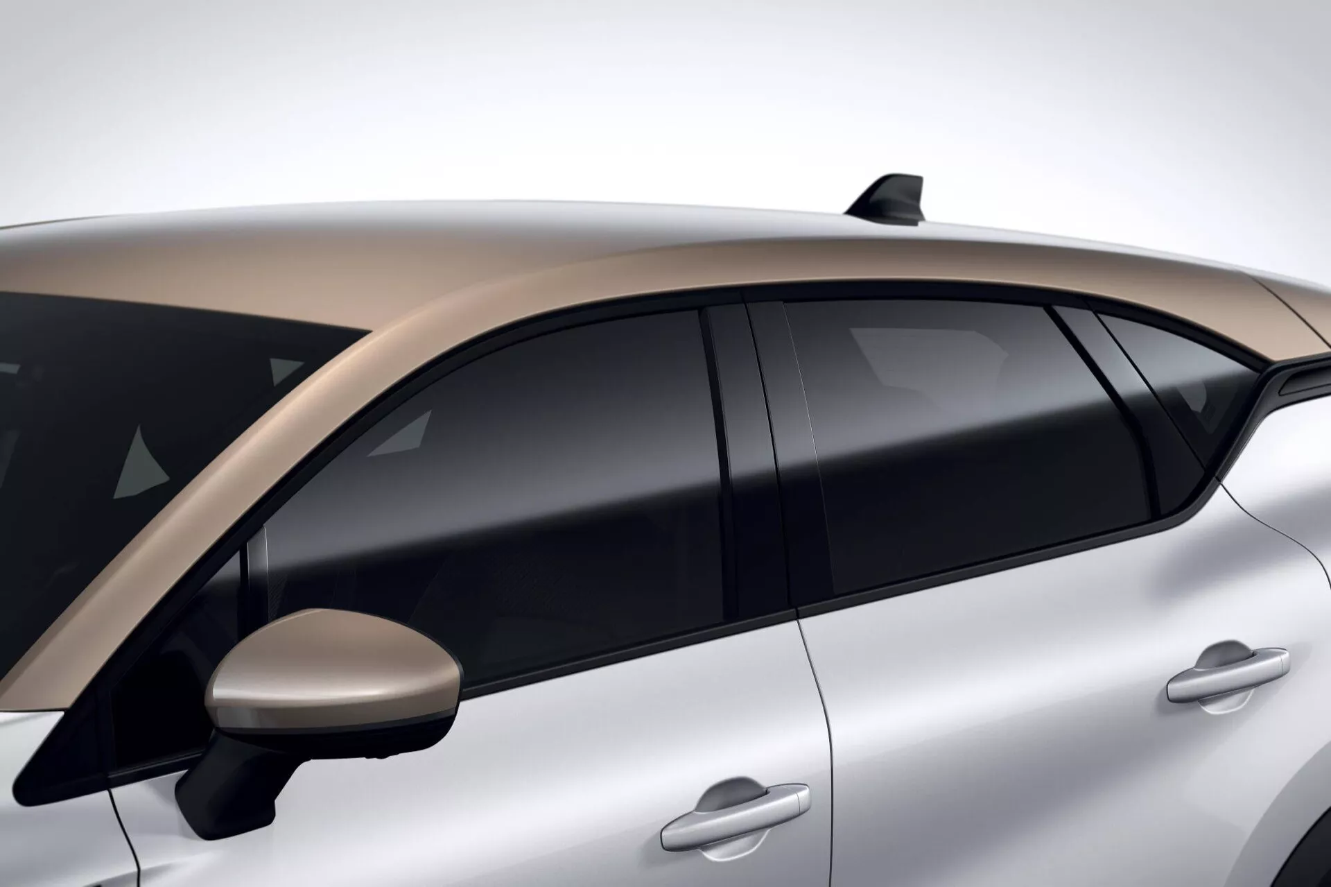 Zbliżony boczny widok Renault Captur 2024 II-Facelift pokazujący aerodynamiczne klamki drzwi, przyciemniane szyby, dwukolorowy dach, strumieniowe lusterko boczne, antenę w kształcie płetwy rekina i metaliczne srebrne wykończenie