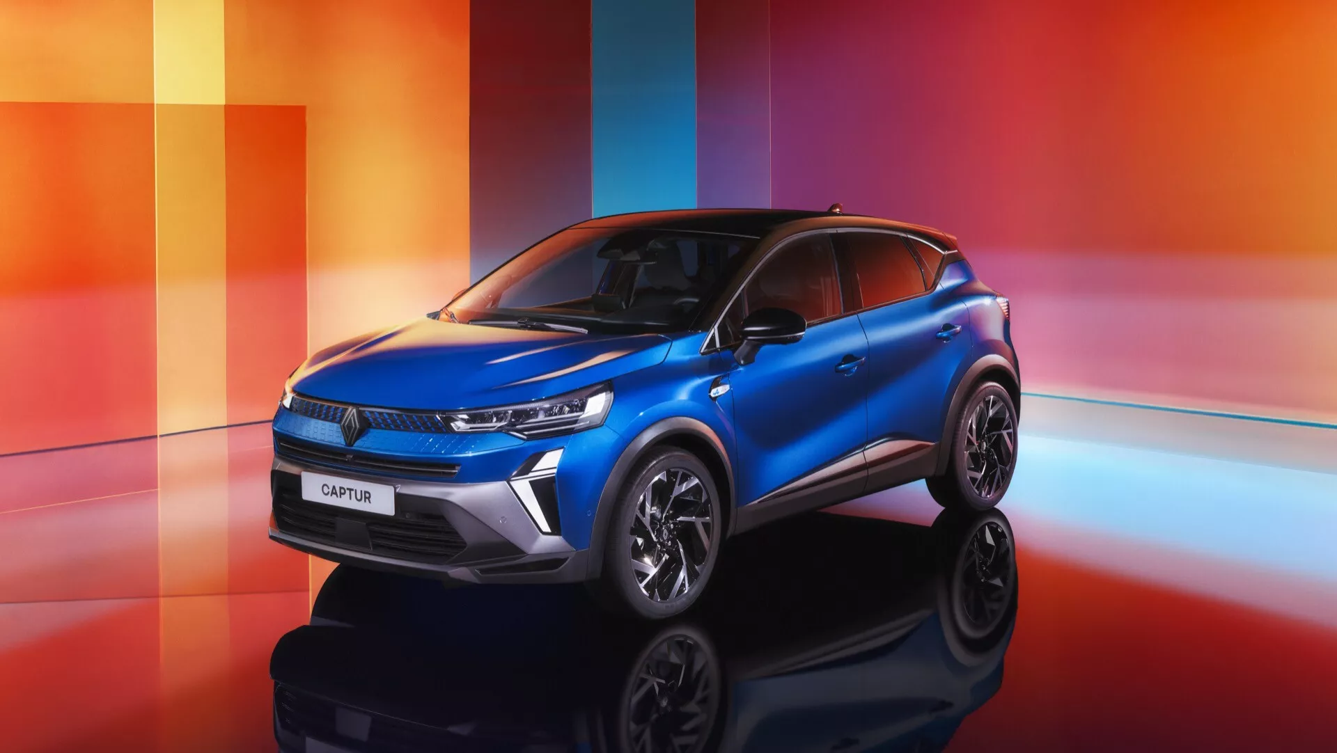 Renault Captur 2024 (II Facelift) zaprezentowany na kolorowym, geometrycznym tle w odcieniach pomarańczowym, czerwonym i fioletowym, podkreślając jego nowoczesny design SUV, smukłe diody LED, poziomą atrapę z emblematem marki, wklęsły kaptur dla lepszej aerodynamiki, sportowe felgi aluminiowe z wieloma szprychami i stylowe malowanie dwukolorowe.