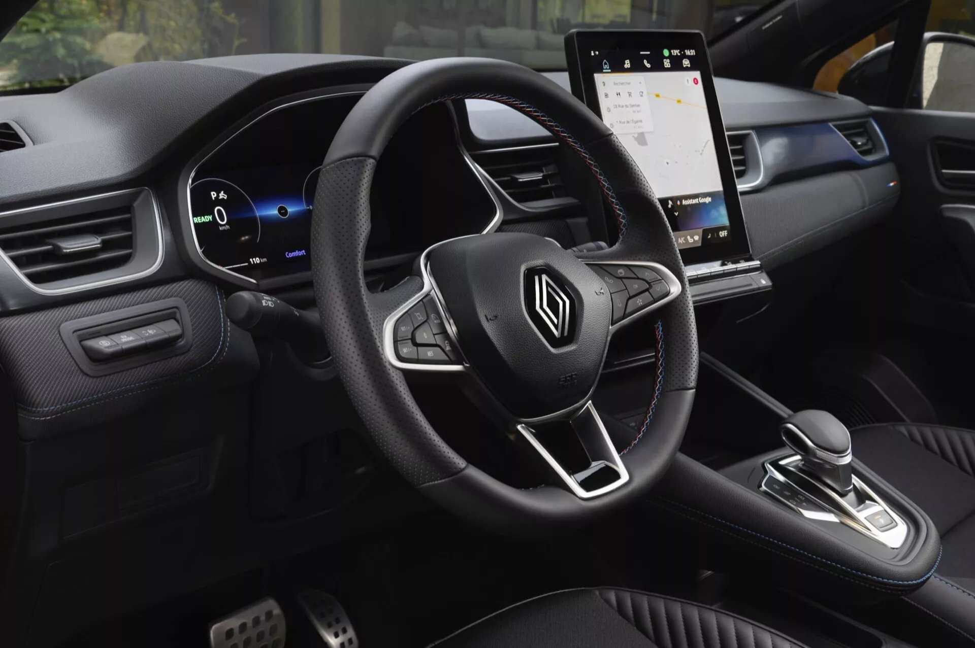 Wnętrze Renault Captur II lifting 2024 z perspektywy pasażera przedniego, prezentujące wielofunkcyjną kierownicę z logo, cyfrowy zestaw wskaźników, ekran dotykowy systemu infotainment, gałkę zmiany biegów dla automatycznej skrzyni biegów, dwukolorową deskę rozdzielczą z miękkimi materiałami i dekoracyjnymi szwami oraz sportowe pedały, podkreślające nowoczesny design skoncentrowany na wygodzie, komforcie i technologii.