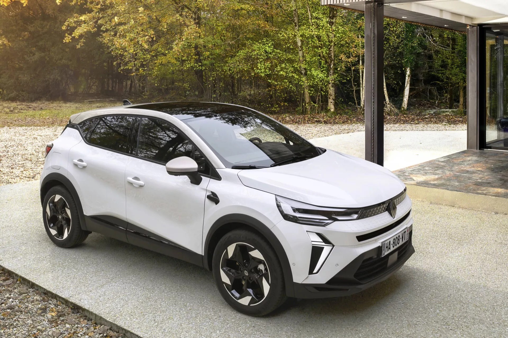 Renault Captur II po liftingu 2024 w kolorze białym, prezentujący dynamiczny grill, reflektory LED i elegancki aerodynamiczny kształt z czarnymi nadkolami i charakterystycznymi alufelgami, zaparkowany na brukowanym obszarze obok modernistycznego budynku z fasadą szklaną