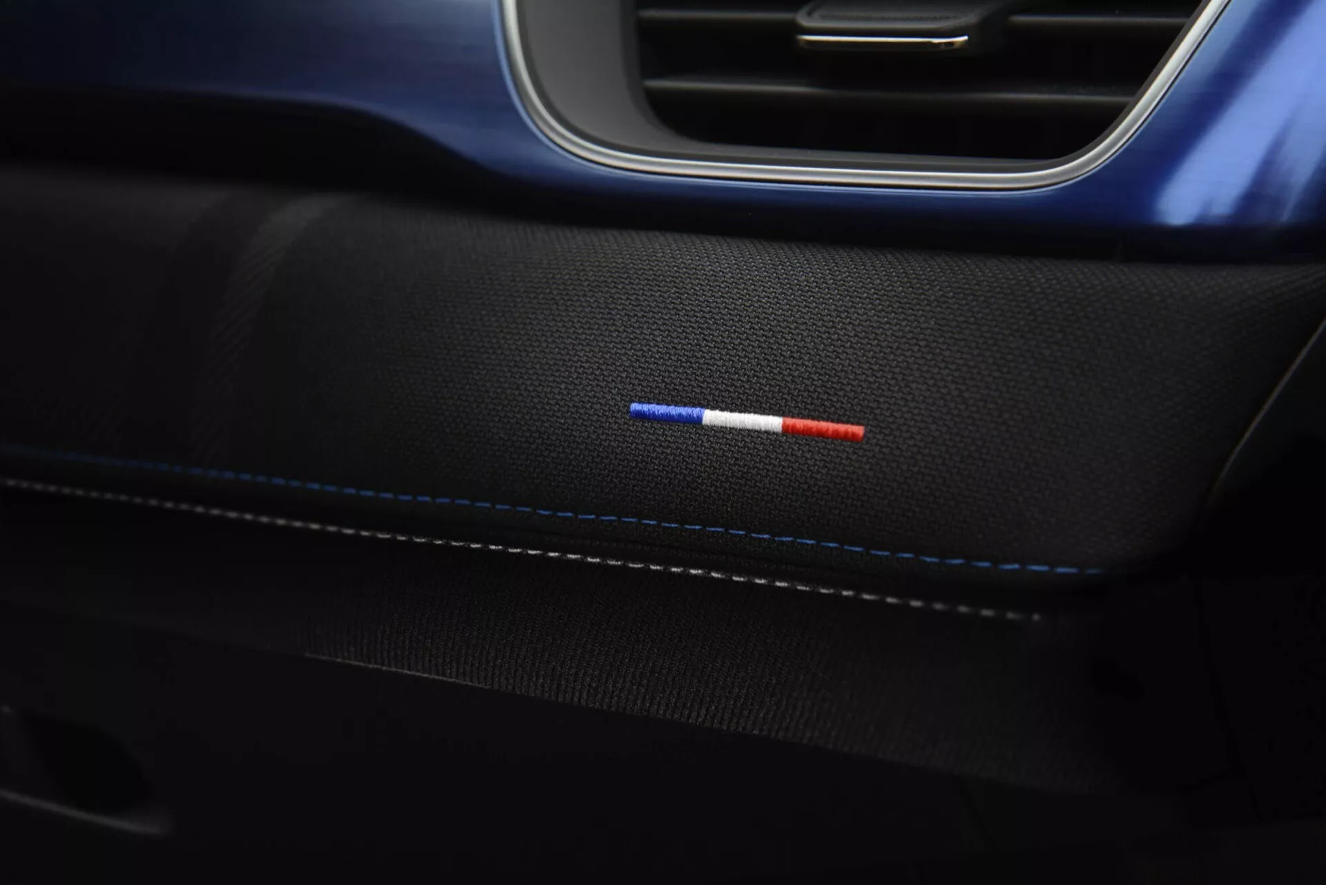 Zbliżenie na panel drzwiowy wnętrza Renault Captur 2024 z subtelnymi szwami na premium czarnej skórze, dwukolorowe oświetlenie ambientowe w kolorze czerwonym i niebieskim, oraz eleganckie czarno-niebieskie wykończenie, prezentujące eleganckie detale projektowe i zaawansowaną technologię oświetlenia