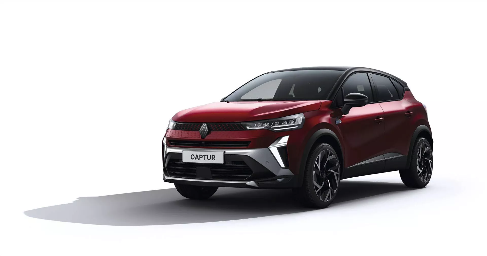 Model Renault Captur po liftingu 2024 w niskim ujęciu czołowo-bocznym ukazujący reflektory LED, dynamiczne linie nadwozia oraz wieloramienne felgi aluminiowe na prostym szarym tle