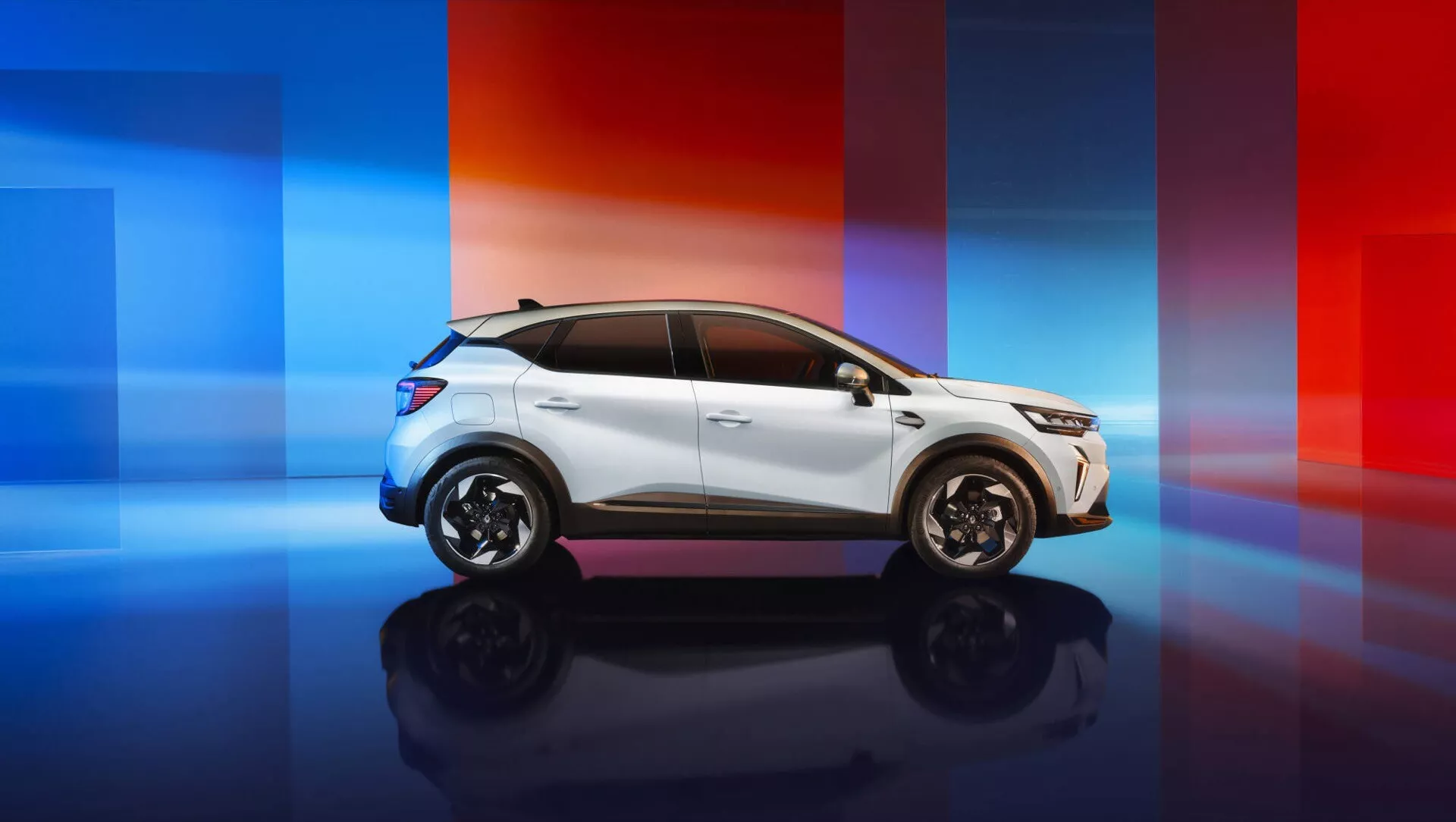 Renault Captur II facelifting 2024 sfotografowany z profilu na tle nowoczesnego gradientu od niebieskiego do czerwonego, prezentujący aerodynamiczne lusterka boczne, wpuszczone klamki, skomplikowane alufelgi, opływowe szyby i sportową linię dachu.