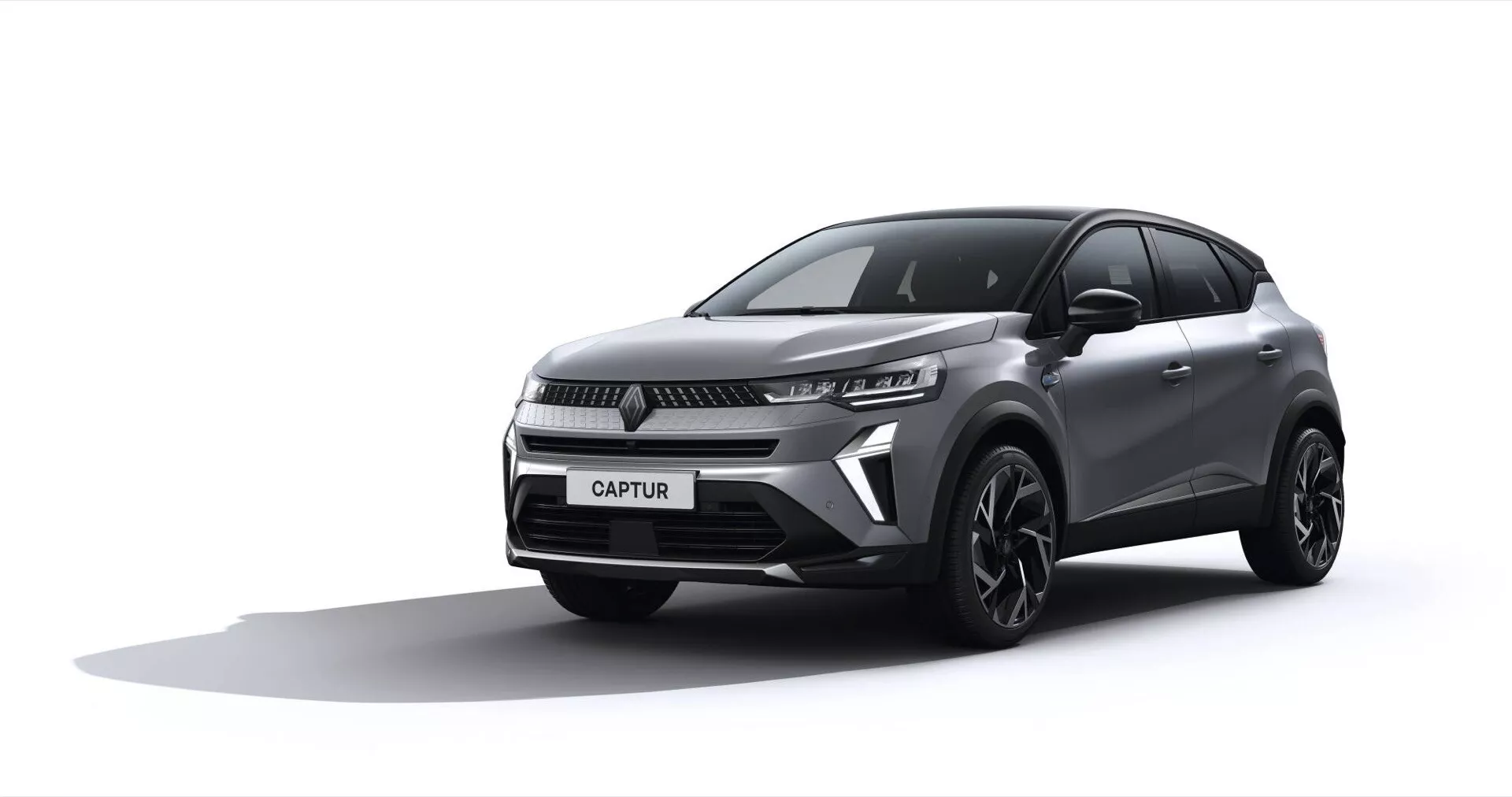 Renault Captur 2024 (II-Facelift) prezentowany w środowisku studyjnym, pokazujący przód i bok w trzech czwartych, aby podkreślić przedni grill, eleganckie reflektory LED, wyrzeźbioną maskę i stylowe koła ze stopu przeciwko tłu zanikającemu z białego do jasnoszarego