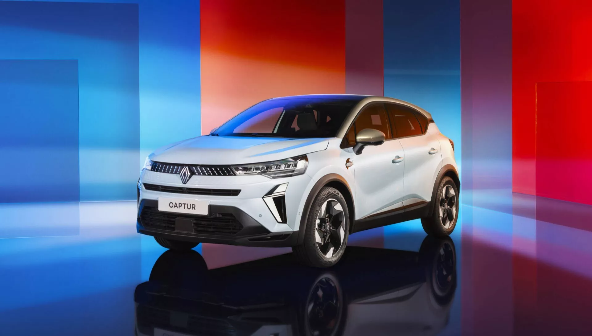 Facelifting Renault Captur II 2024 przedstawiający trzy czwarte widoku frontowego białego kompaktowego SUV-a na cyfrowo stworzonym tle z czerwono-niebieskimi gradientami, podkreślający nowoczesne reflektory LED, wyraźną kratę z logo producenta, dynamiczne linie, rzeźbione linie maski, elegancką linię dachu i duże koła z lekkich stopów o wielu szprychach.