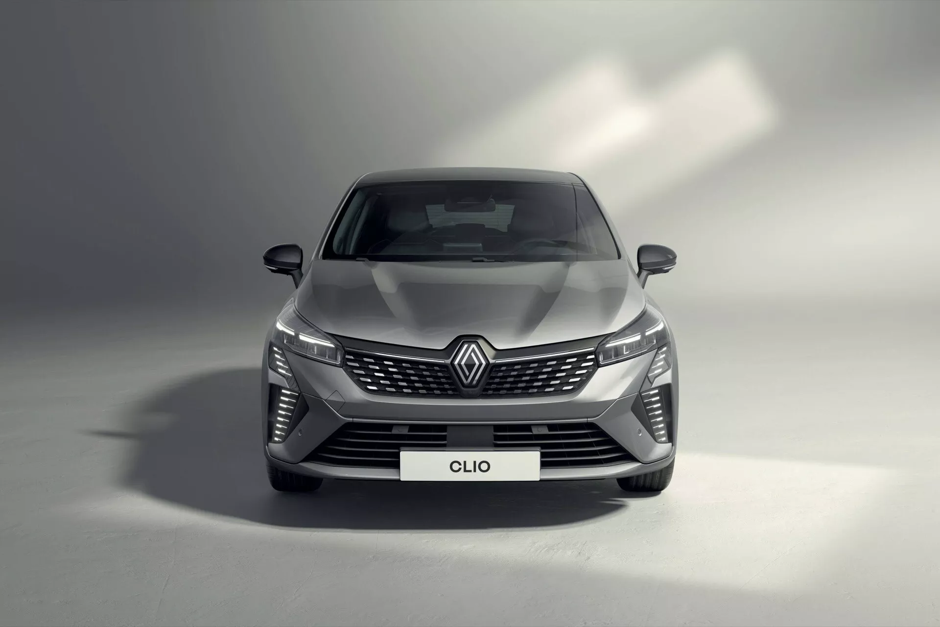 Przedni widok Renault Clio V-facelift 2023 przedstawiający reflektory LED, szeroką grilę z wzorem w romby z centralnie umieszczonym emblematem marki, aerodynamicznie zaprojektowany zderzak z wlotami powietrza i wysokiej jakości metaliczne wykończenie w ustawieniu studyjnym