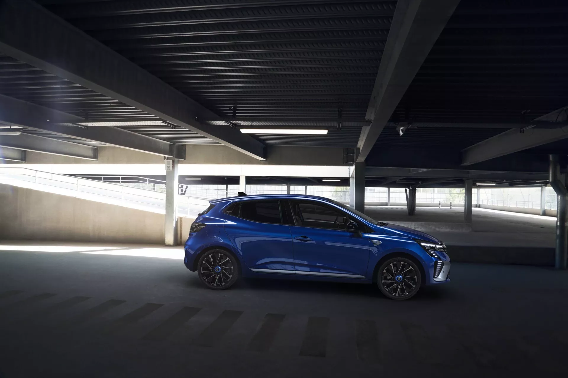 Niebieski hatchback Renault Clio V-facelift 2023 zaparkowany pod kątem w słabo oświetlonym garażu, podkreślający jego elegancki wygląd, felgi aluminiowe i zintegrowane funkcje technologiczne