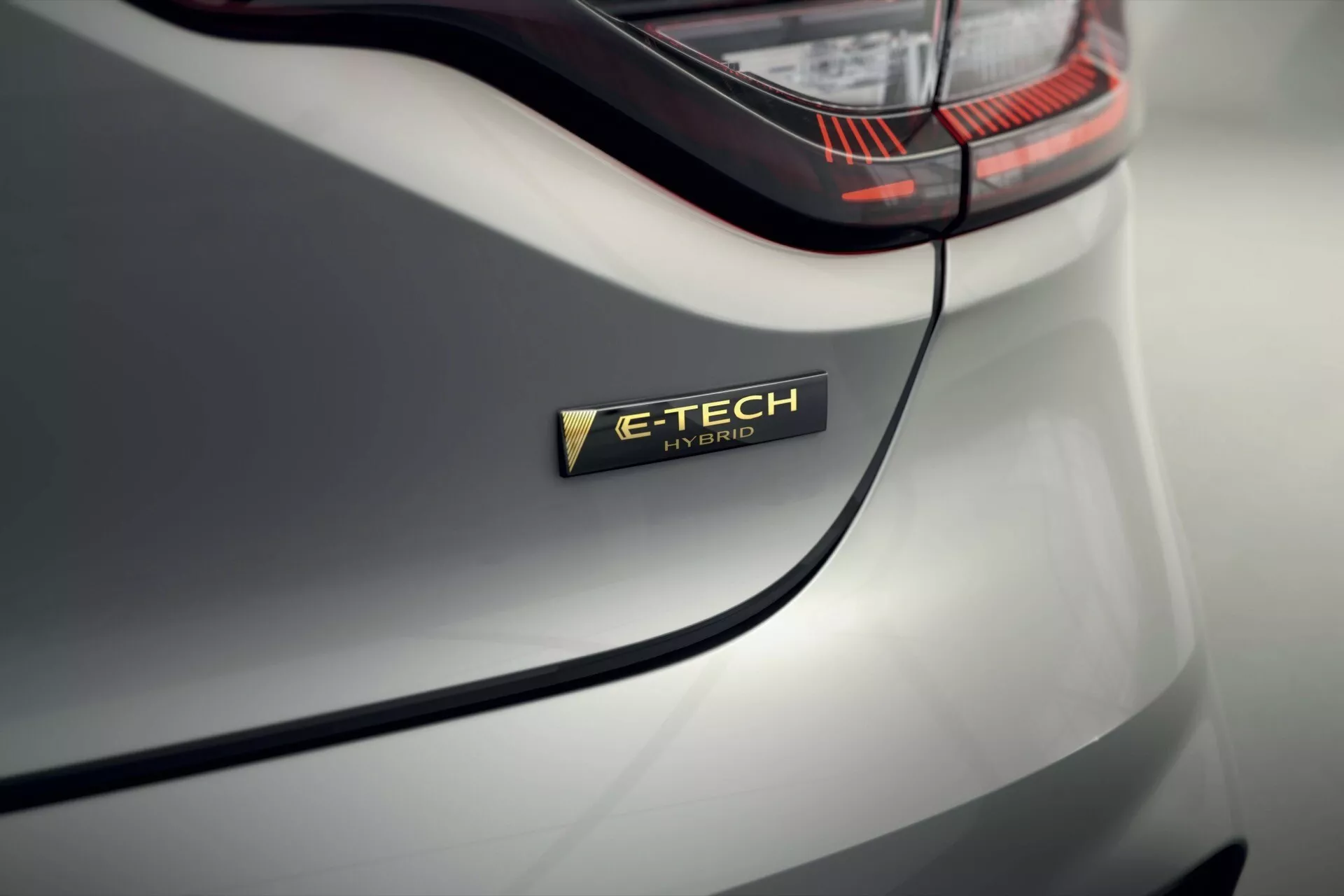 Zbliżenie na odznakę E-TECH Hybrid w Renault Clio V-Facelift 2023 na tylnej części błotnika, ukazujące technologię hybrydową pojazdu i elegancki design karoserii w jasnoszarym kolorze