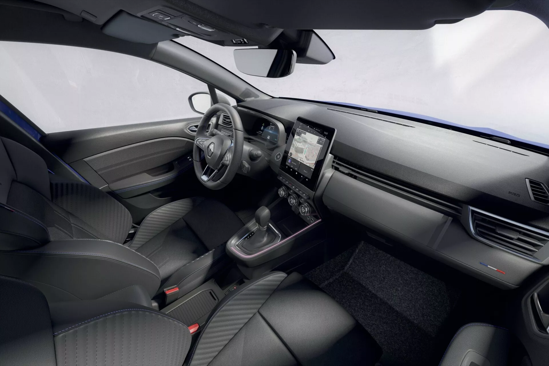 Wnętrze Renault Clio facelift 2023 przedstawiające deskę rozdzielczą, kierownicę z zamontowanymi sterowaniami, cyfrowy zestaw wskaźników, system infotainment dotykowy, interfejs klimatyzacji, selektor zmiany biegów i przednie siedzenia z podwyższonej perspektywy po stronie kierowcy.