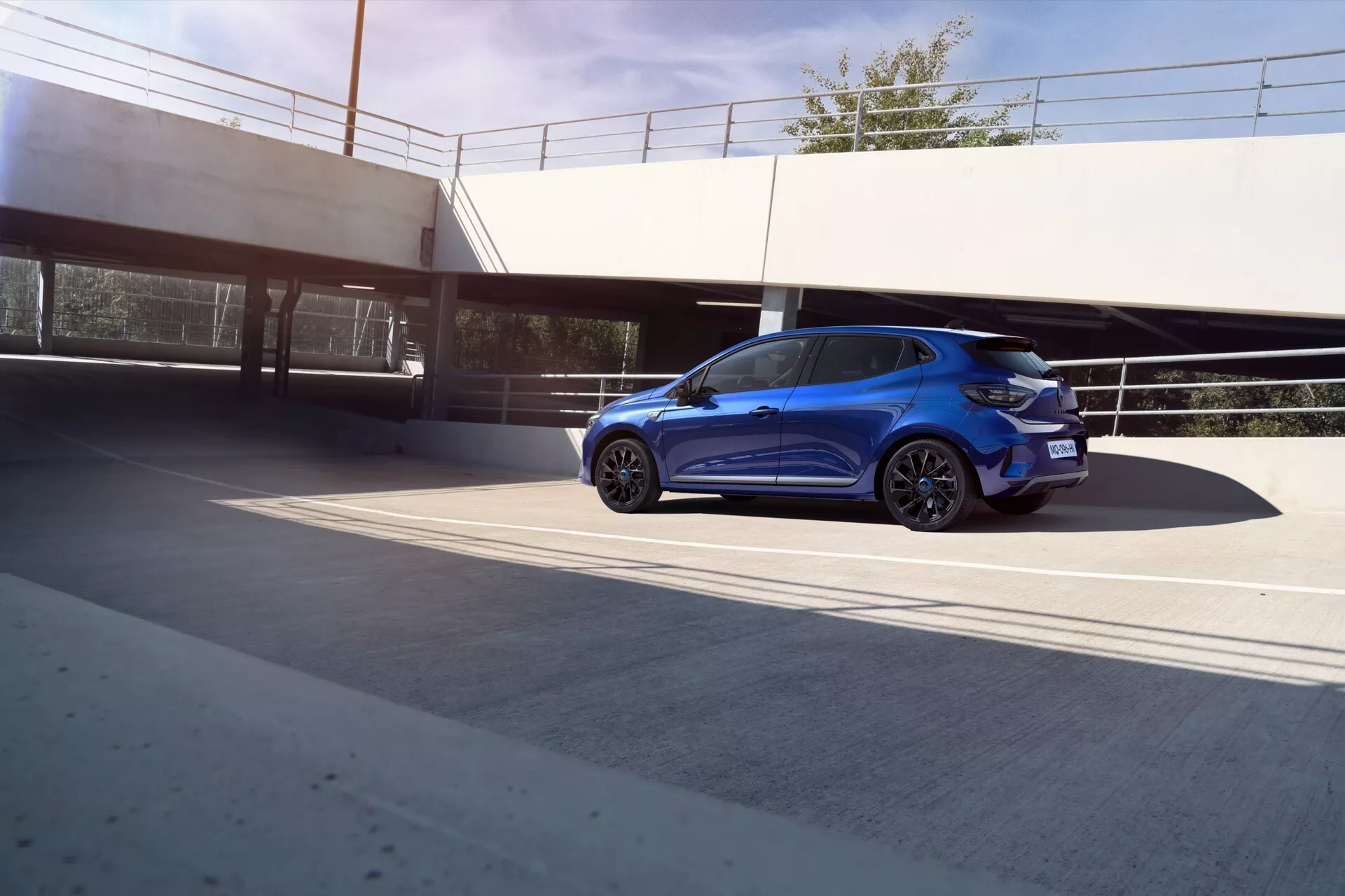 Renault Clio V-Facelift 2023, metaliczny niebieski, prezentujący nowoczesne cechy z ledowymi światłami, felgami aluminiowymi, przyciemnianymi szybami i aerodynamicznym designem z perspektywy trzy czwarte z tyłu w miejskim otoczeniu