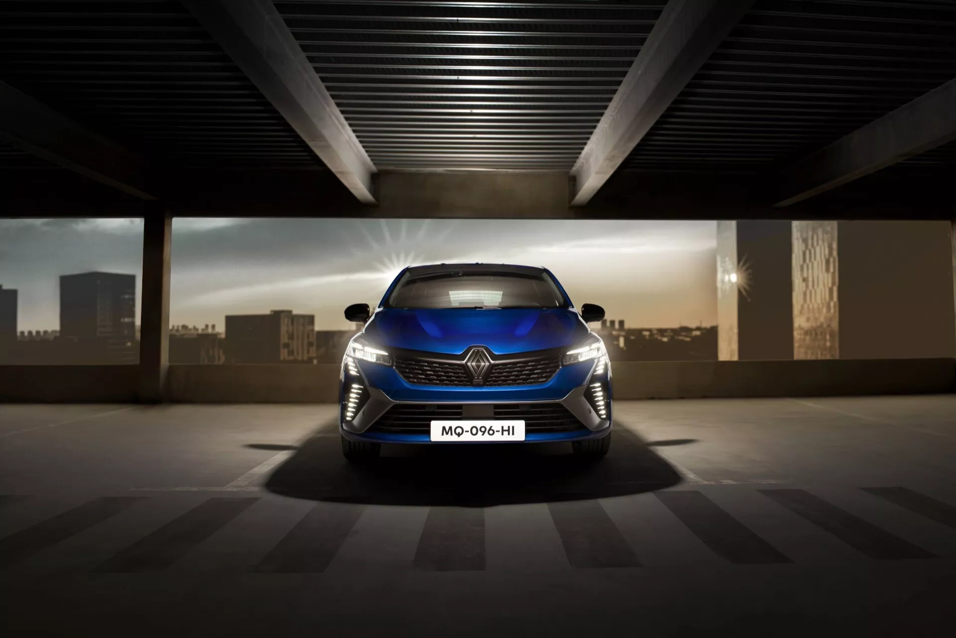 Zdjęcie przedniej części Renault Clio V-facelift 2023 podkreślające sportową atrapę, reflektory LED i aerodynamiczny design na oświetlonym sztucznie parkingu