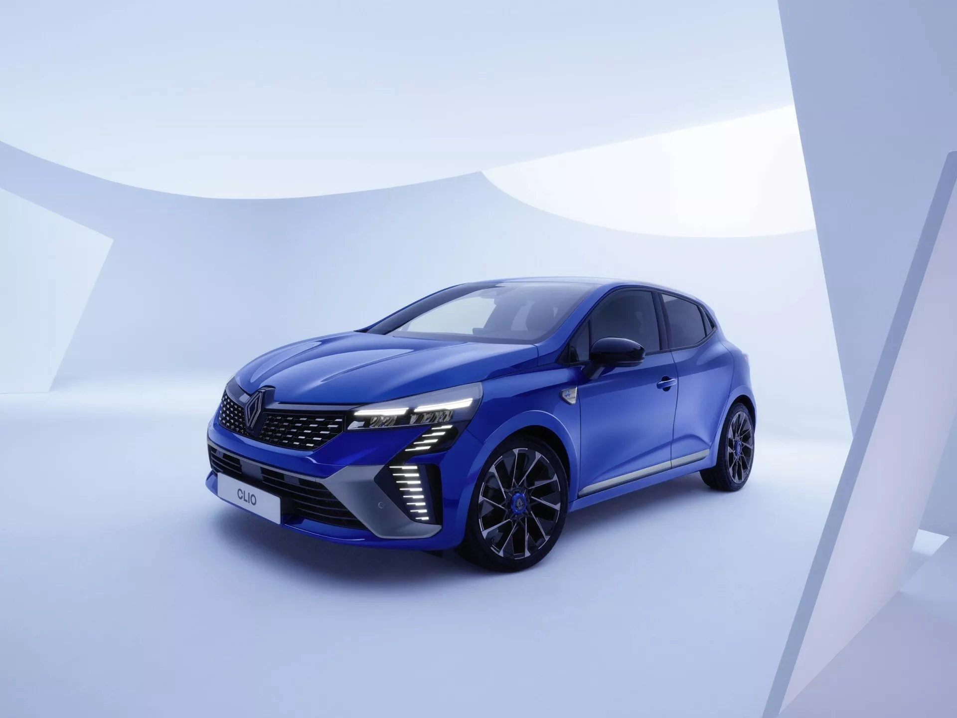 Renault Clio V-Facelift 2023 w widoku z przodu trzy czwarte, z reflektorami LED, charakterystycznym wzorem grilla, zaawansowanymi systemami wspomagania kierowcy i eleganckim, aerodynamicznym designem na stylowym minimalistycznym tle