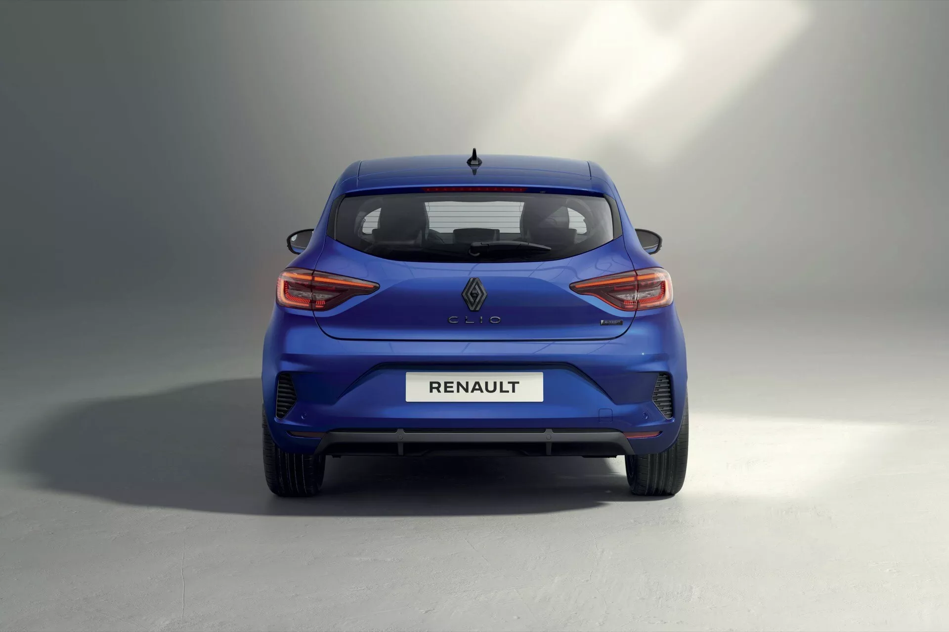 Tylny widok Renault Clio V-facelift 2023 prezentujący nowoczesny design niebieskiego hatchbacka i tylne światła LED, w przestronnym studio z tłem gradientu szaro-białego.