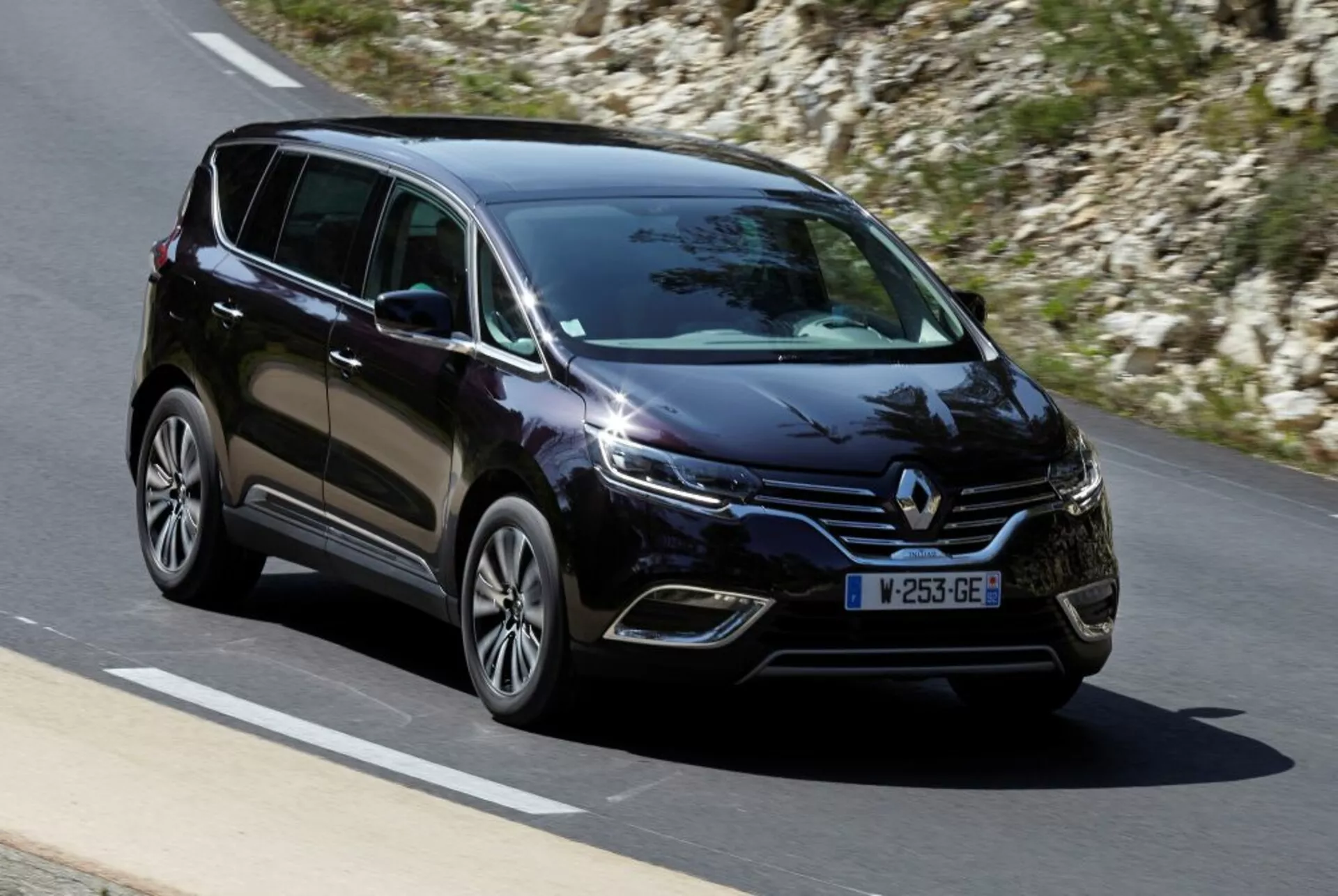 Minivan Renault Espace 2015 w ruchu na wybrukowanej drodze, widok z przodu i z boku pokazujący oświetlenie LED, koła ze stopów i nowoczesne cechy konstrukcyjne
