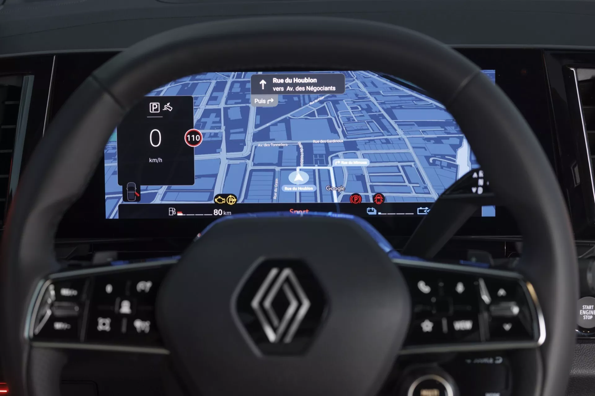 Widok wnętrza Renault Espace VI 2023 z perspektywy miejsca kierowcy, podkreślający nowoczesną kierownicę o płaskim dnie z wielofunkcyjnymi przyciskami oraz szerokoekranowy cyfrowy panel wskaźników z wbudowanym systemem nawigacji GPS, wykrywaniem ograniczeń prędkości i wyświetlaniem poziomu energii dla napędu hybrydowego lub elektrycznego, plus wyświetlacz HUD projekcyjny prędkości i wskazówek nawigacyjnych