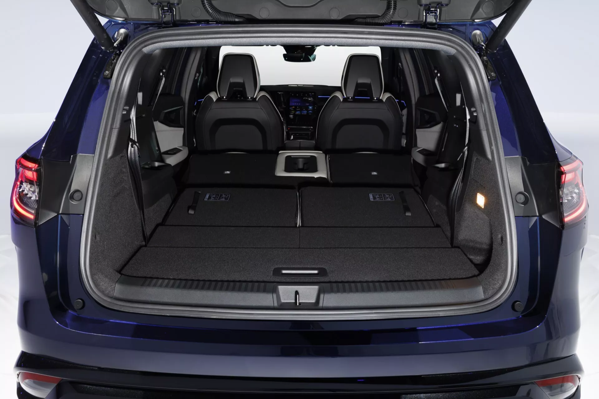 Widok przestrzeni bagażowej Renault Espace VI 2023 z otwartymi tylnymi drzwiami pokazujący pojemny bagażnik, płaską powierzchnię załadunku, punkty mocowania pokrywy bagażu, boczne komory przechowywania, wyściełany dywanem wnętrze, uchwyty na kubki i oświetlenie