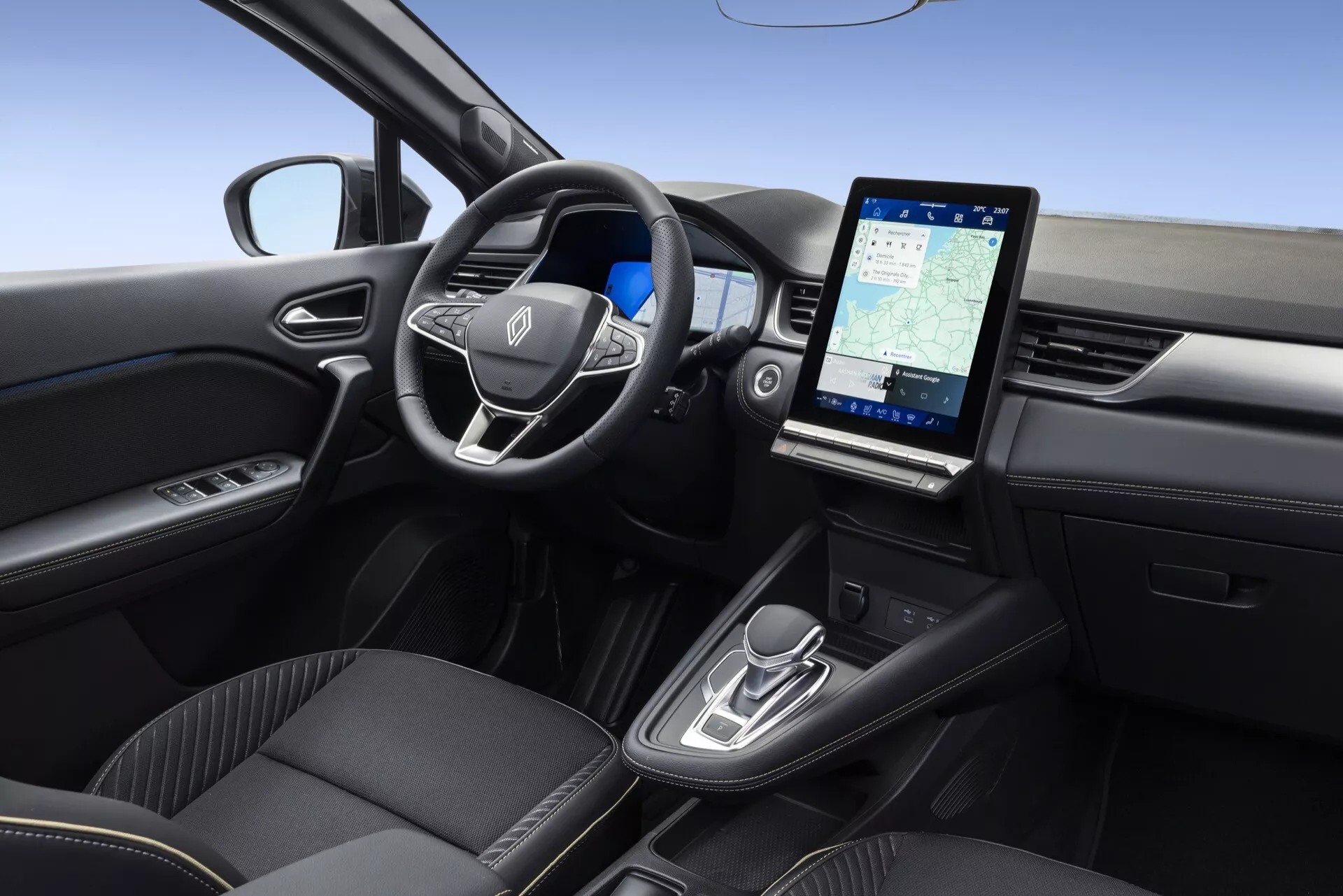 Wnętrze Renault Symbioz model 2024, ukazane z podniesionego, lekko prawego kąta. Zawiera wielofunkcyjną kierownicę z logo producenta, minimalistyczny kokpit sugerujący cyfrowy wyświetlacz lub head-up display, duży pionowy ekran dotykowy systemu infotainment wyświetlający nawigację, nowoczesne sterowanie automatyczną skrzynią biegów, wysokiej jakości czarne fotele z prestiżową tapicerką oraz drzwi kierowcy z przyciskami sterującymi elektrycznymi szybami.