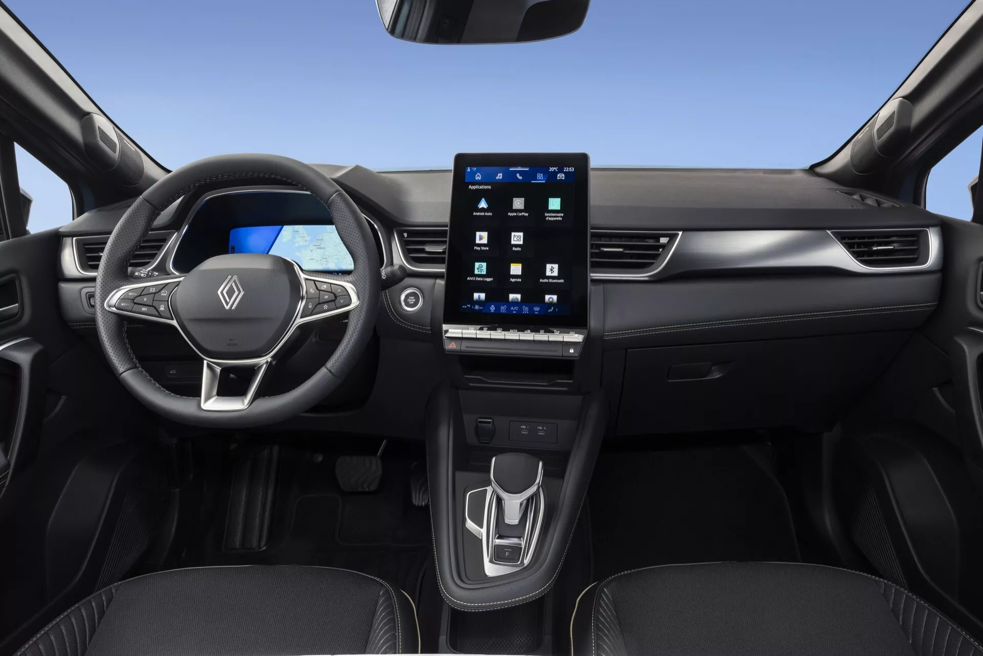 Widok wnętrza Renault Symbioz 2024 z przedniego siedzenia pasażera, prezentujący wielofunkcyjną trójramienną kierownicę z wbudowanymi kontrolkami, jasny cyfrowy zestaw wskaźników oraz duży pionowy ekran dotykowy systemu infotainment zintegrowany w konsoli centralnej. Czysta i nowoczesna konsola środkowa obejmuje minimalistyczny panel sterowania dotykowego do regulacji klimatu oraz współczesny elektroniczny selektor biegów, wraz z widocznymi uchwytami na kubki. Pojazd charakteryzuje się eleganckim designem z użyciem wysokiej jakości materiałów i zharmonizowanymi panelami drzwi, kładąc nacisk na zaawansowaną technologię motoryzacyjną, cyfrowe wskaźniki i wygodę użytkownika.