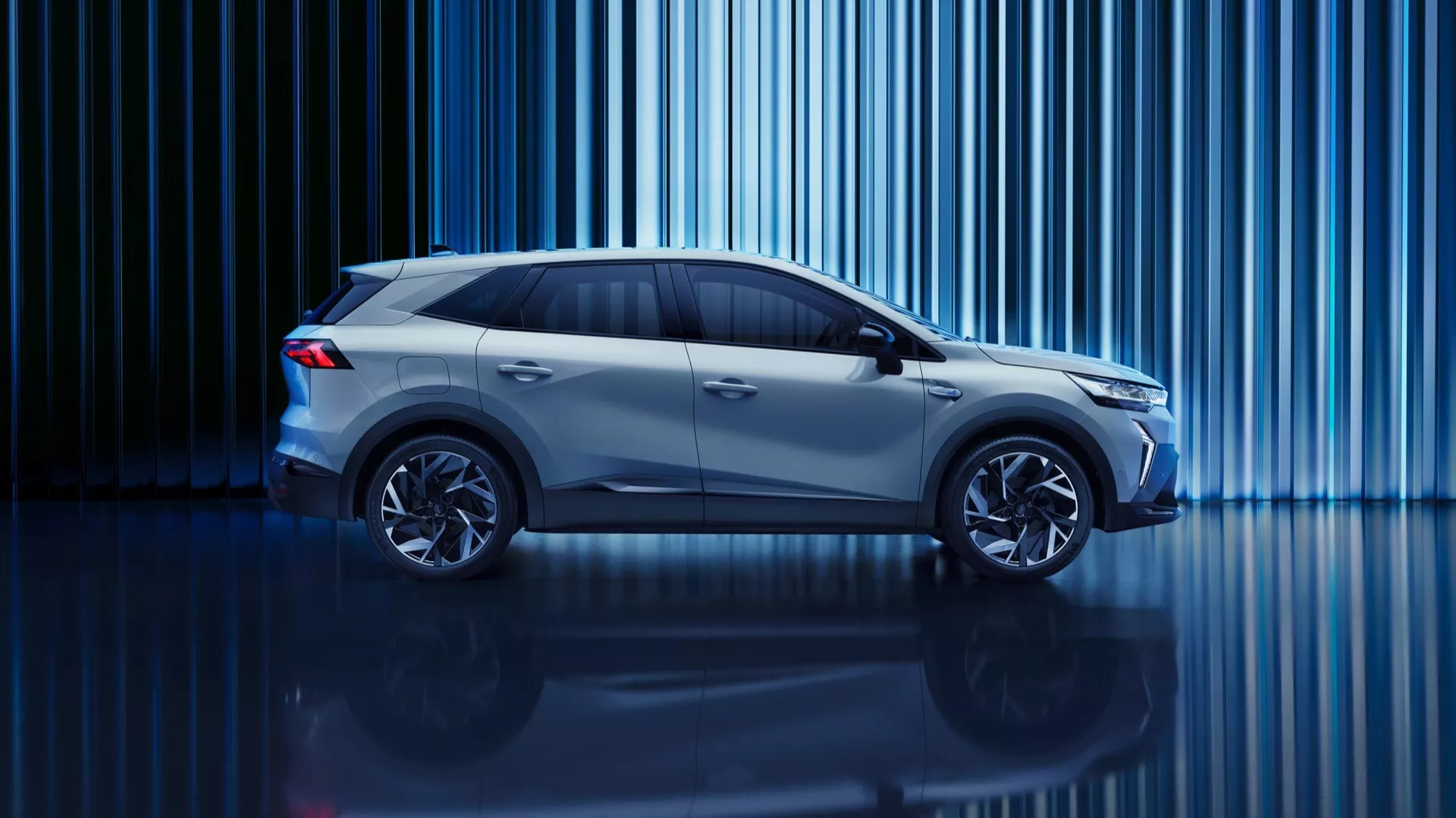 Obraz studyjny Renault Symbioz 2024 (1. generacji) z profilu bocznego. Samochód, kompaktowy SUV lub crossover z podwyższonym prześwitem, jest oświetlony kreatywnym niebieskim światłem. Pionowe smugi świetlne w tle i błyszcząca podłoga dodają nowoczesny, high-techowy klimat. Widoczne są nowoczesne elementy, takie jak aerodynamiczne linie, duże koła i eleganckie lusterka boczne. Przycienione okna boczne sugerują zaawansowane technologie wewnątrz, a design wskazuje na energooszczędną inżynierię, prawdopodobnie elektryczną lub hybrydową.